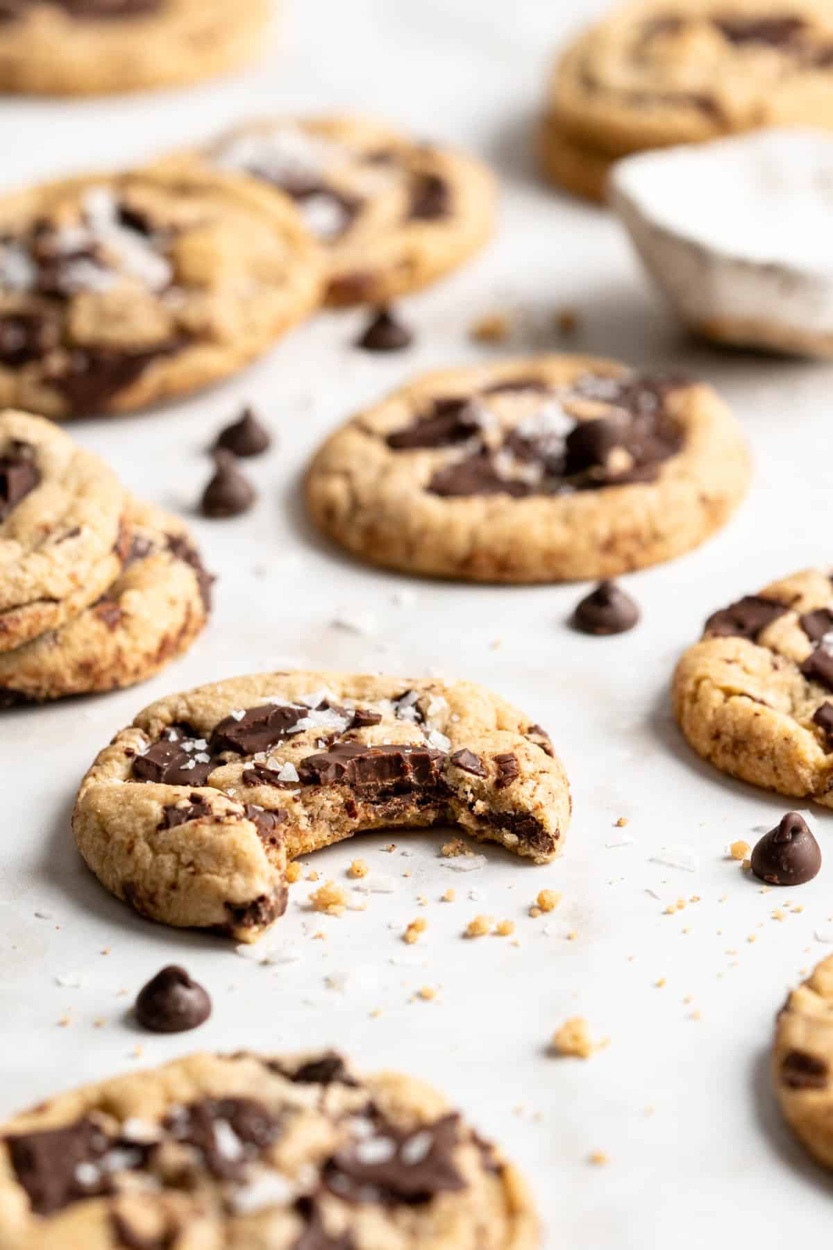 Vegan chocolate chip cookies on parchment paper, one with bite removed
