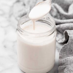 Spoonful of vegan heavy cream spilling into jar of cream