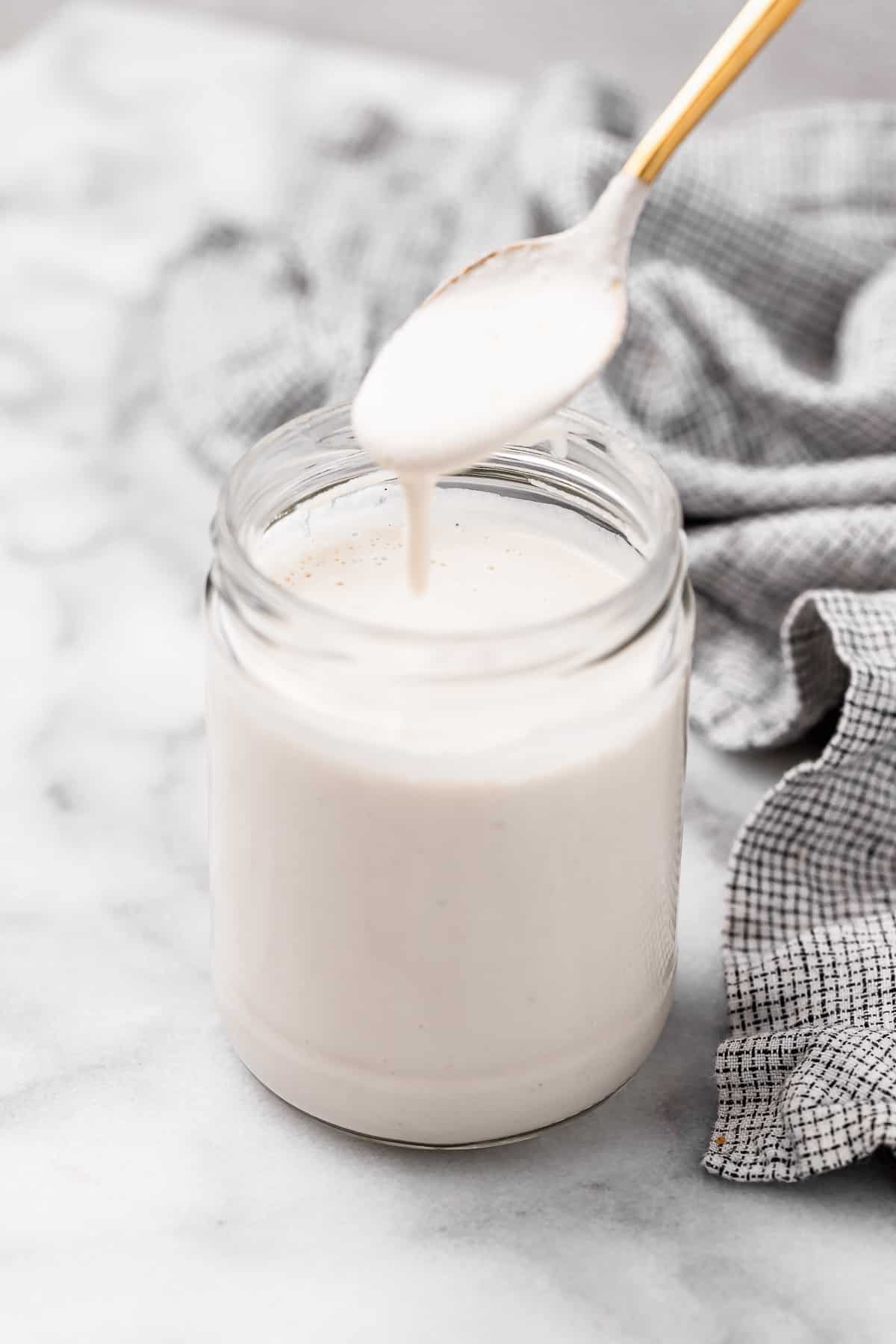 Spoonful of vegan heavy cream spilling into jar of cream