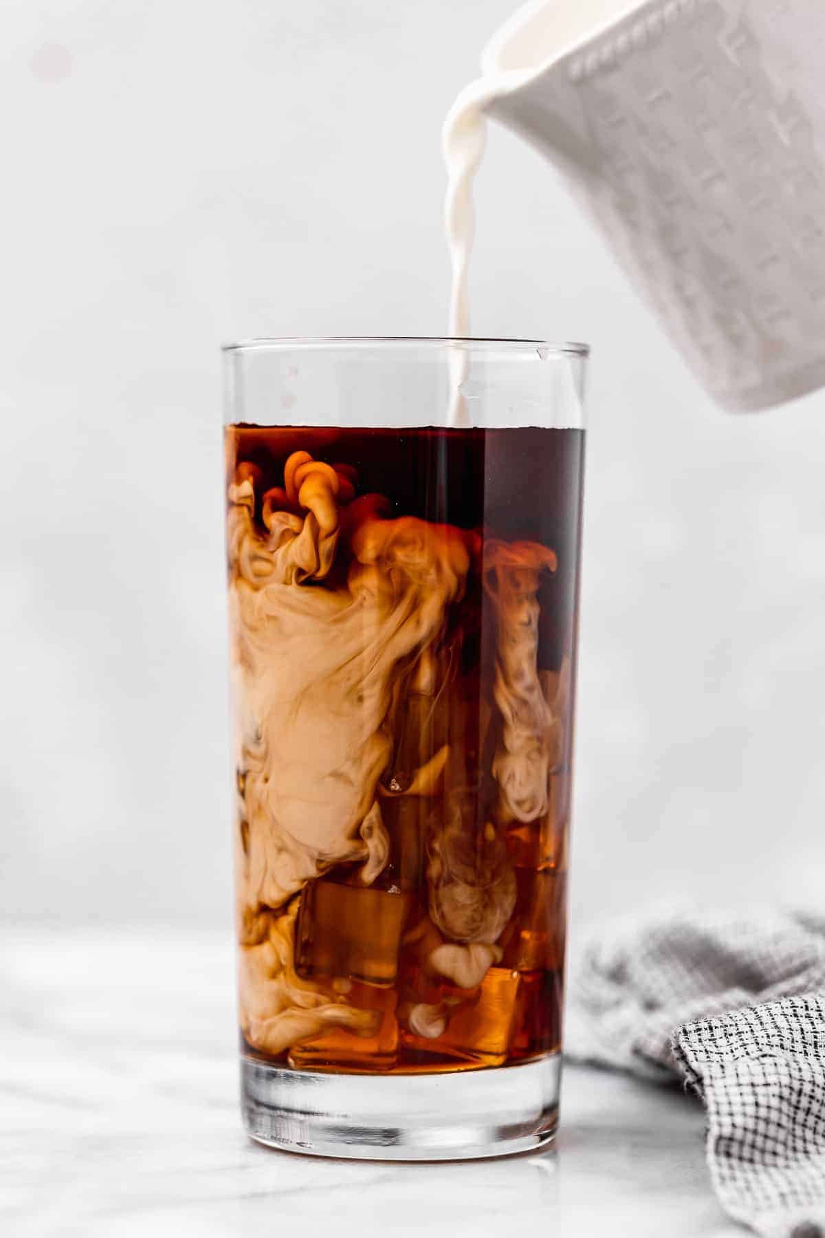 Vegan heavy cream being poured into glass of iced coffee