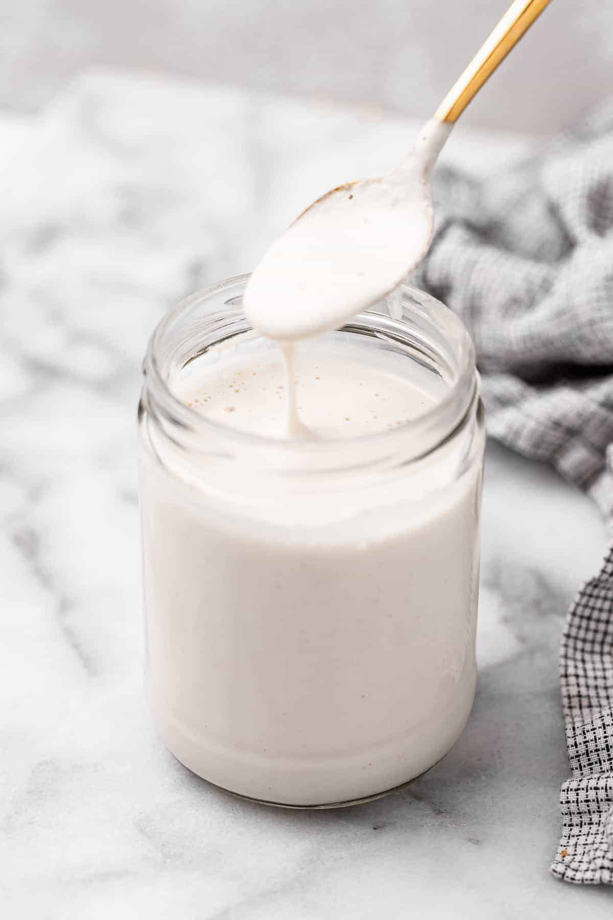 Spoonful of vegan heavy cream held over jar