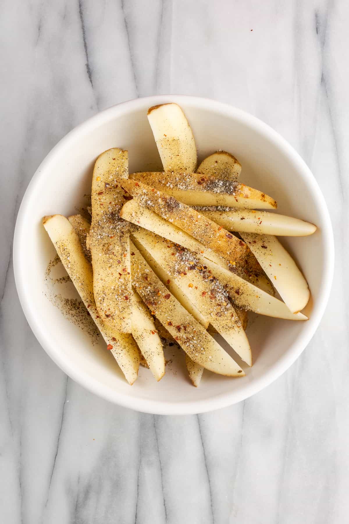 Uncooked potato wedges with seasoning on top