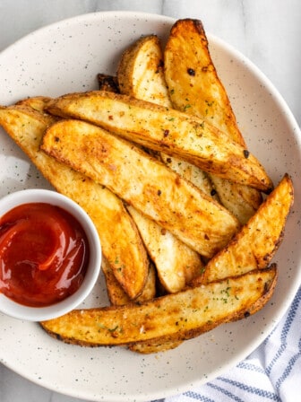 A bowl of potato wedges with a ramekin of ketchup