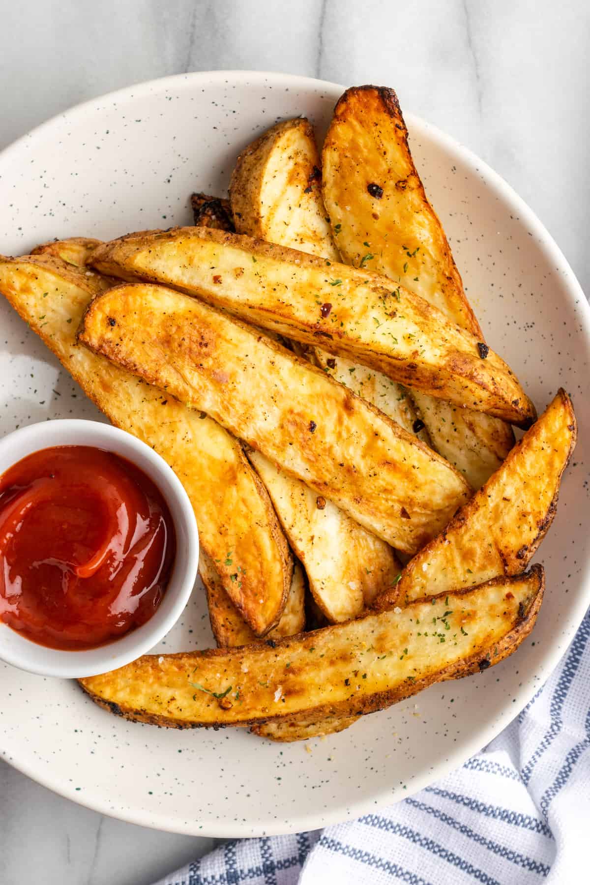 A bowl of potato wedges with a ramekin of ketchup