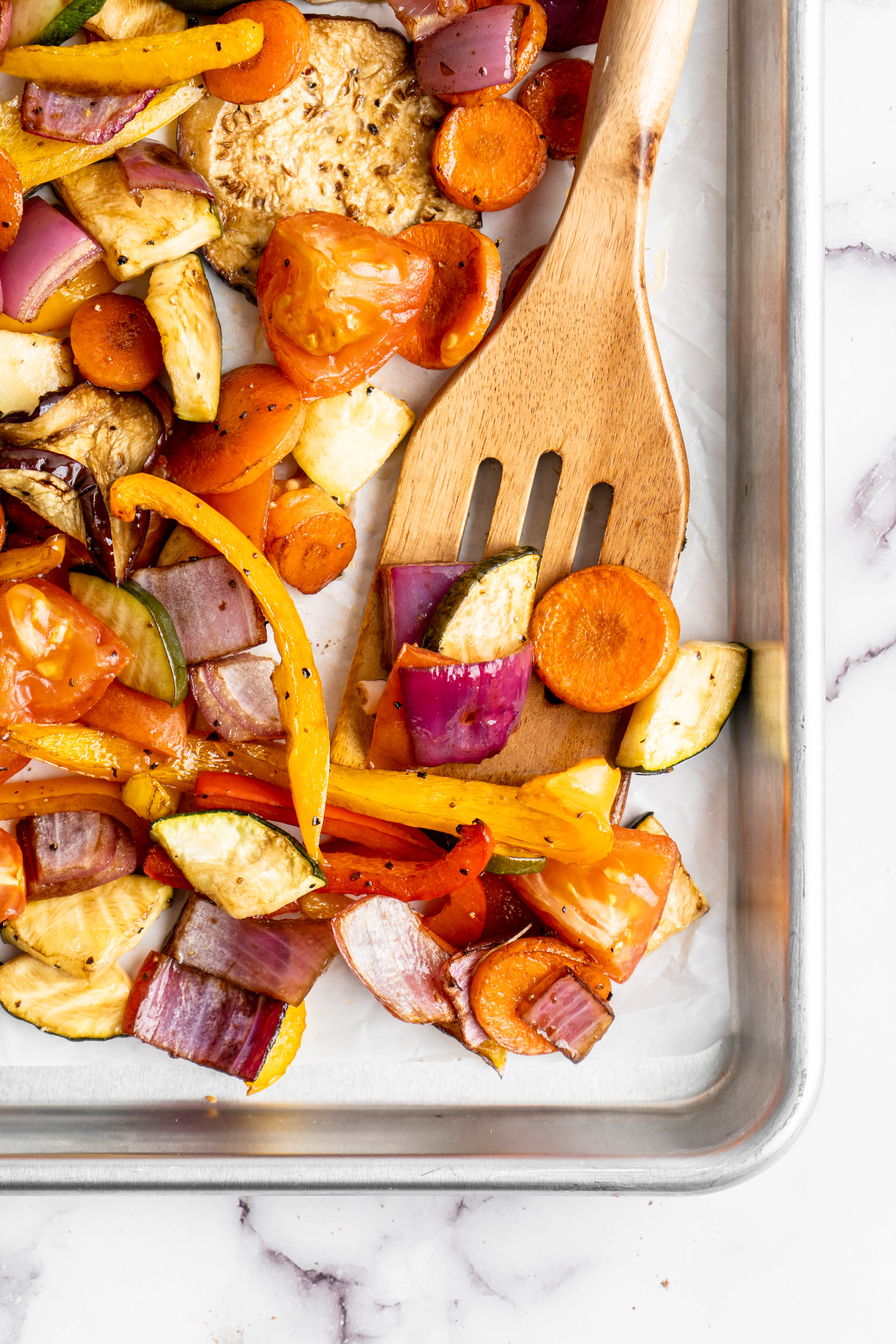 Wooden spoon lifting roasted vegetables from sheet pan