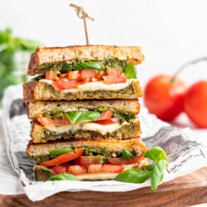 Three stacked vegan caprese sandwiches set on wooden cutting board