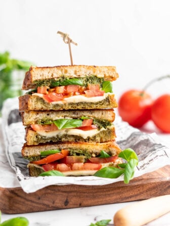 Three stacked vegan caprese sandwiches set on wooden cutting board
