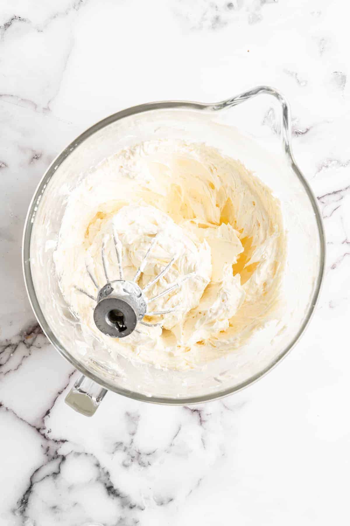Overhead view of vegan butter and cream cheese whipped in glass mixing bowl with whisk attachment