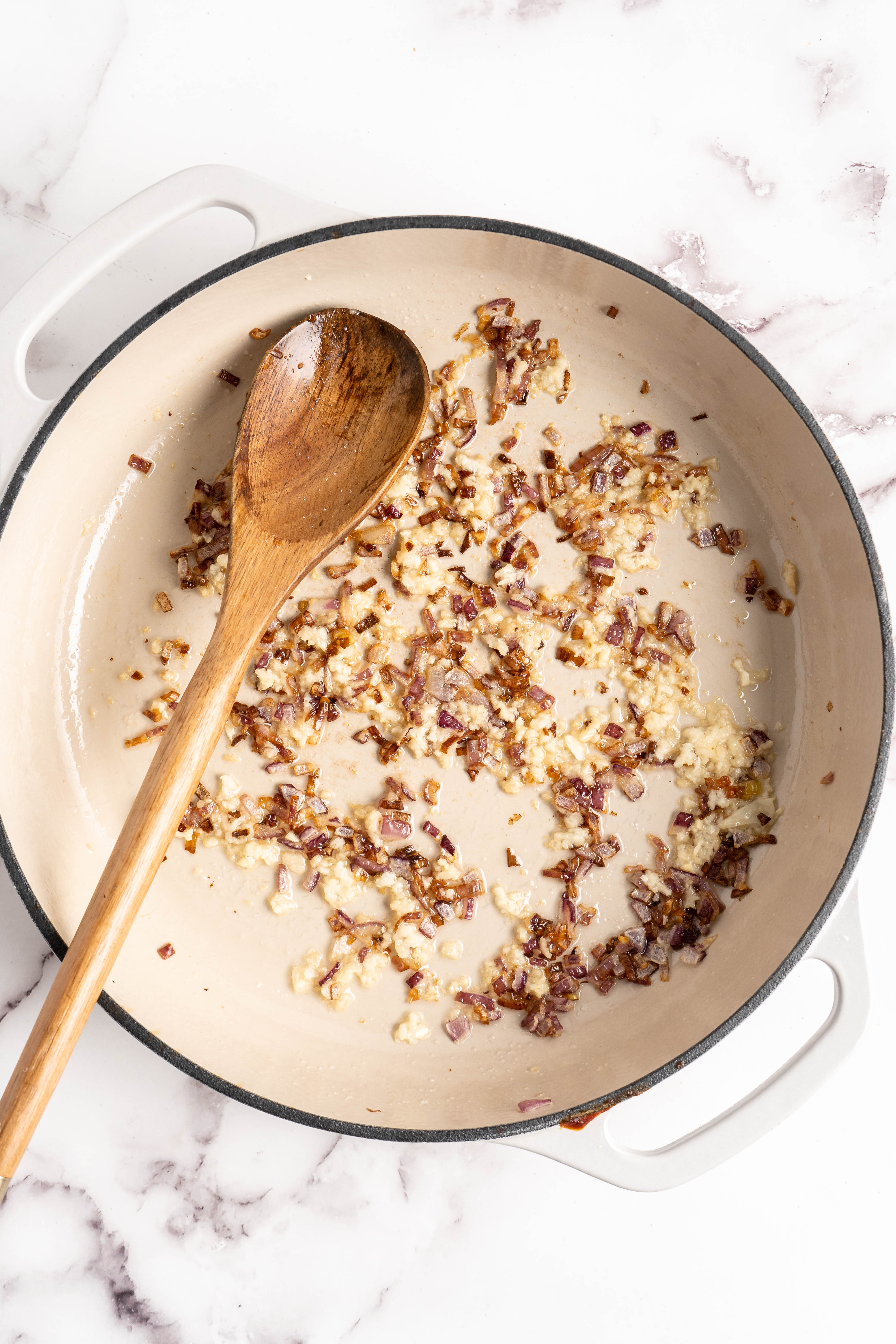 Overhead view of onions and garlic in pan with wooden spoon