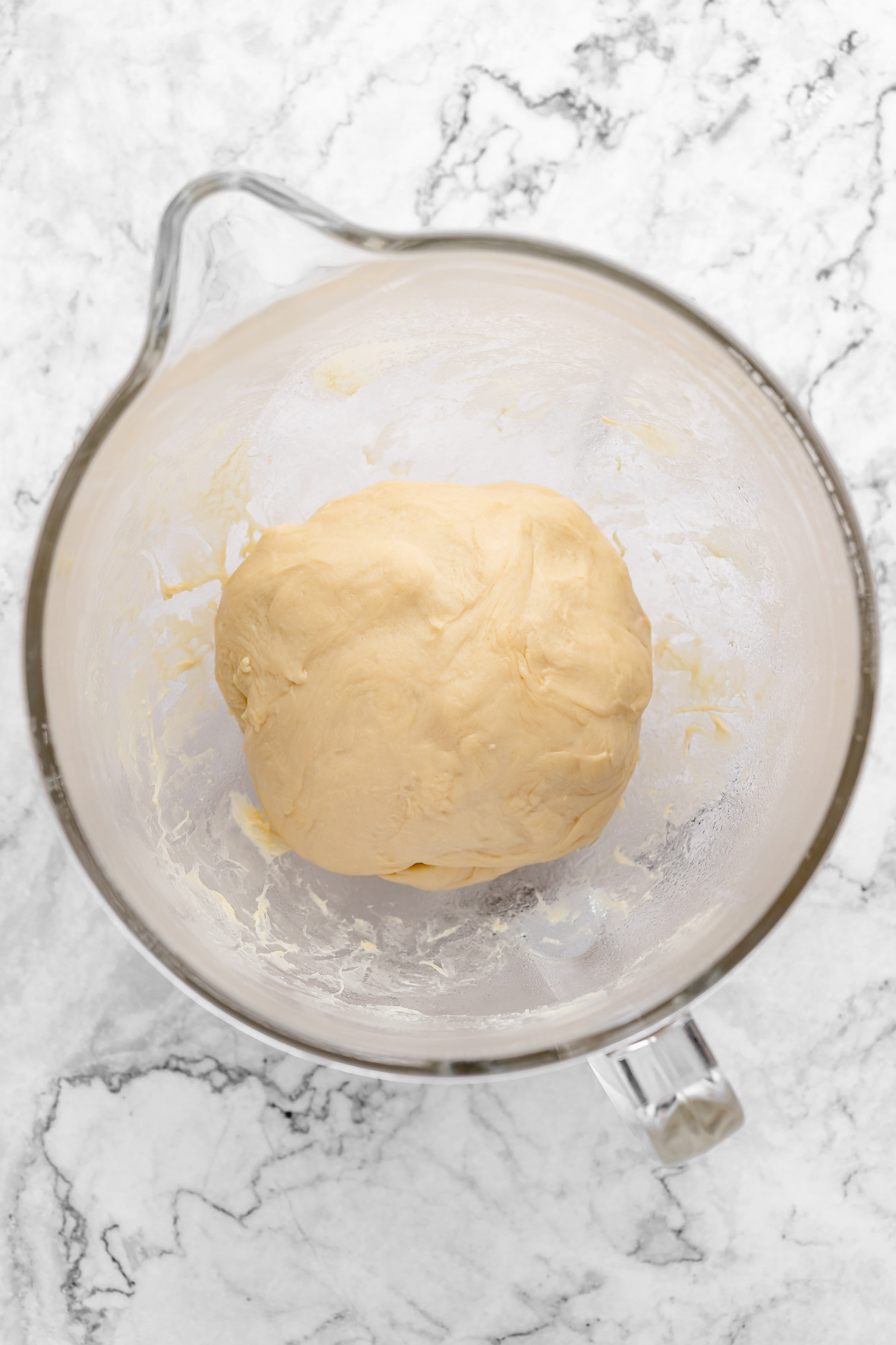 Overhead view of bread dough in glass mixing bowl