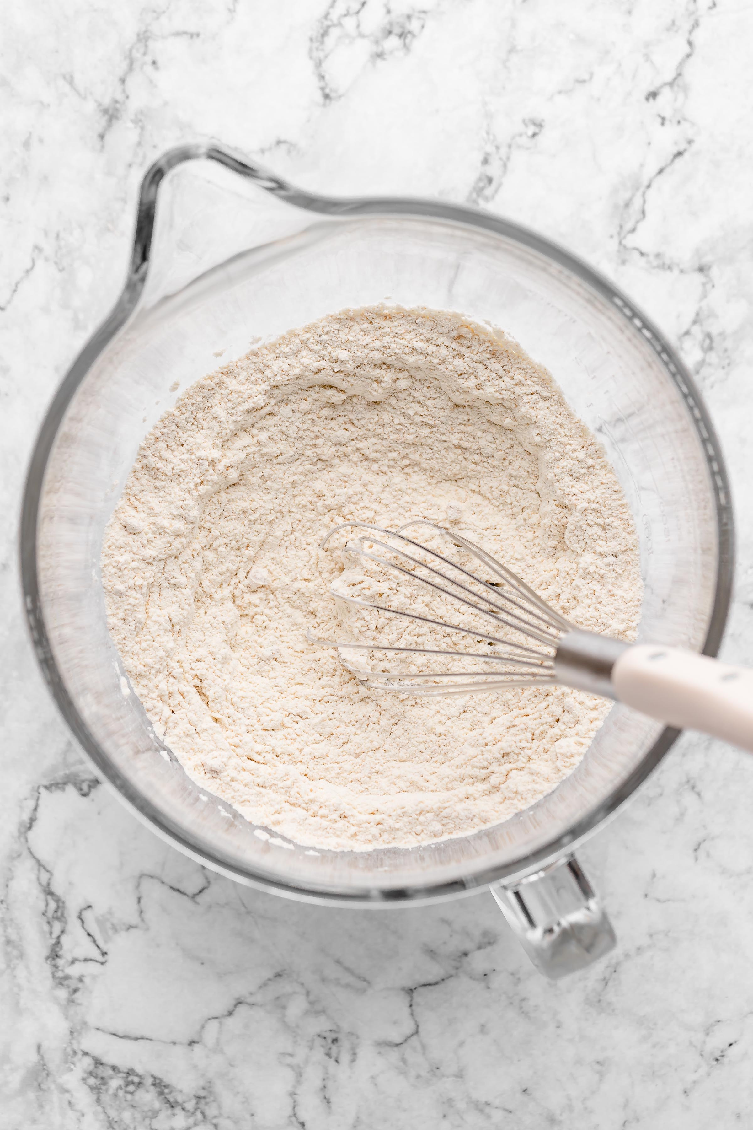 Overhead view of dry bread ingredients in glass mixing bowl with whisk