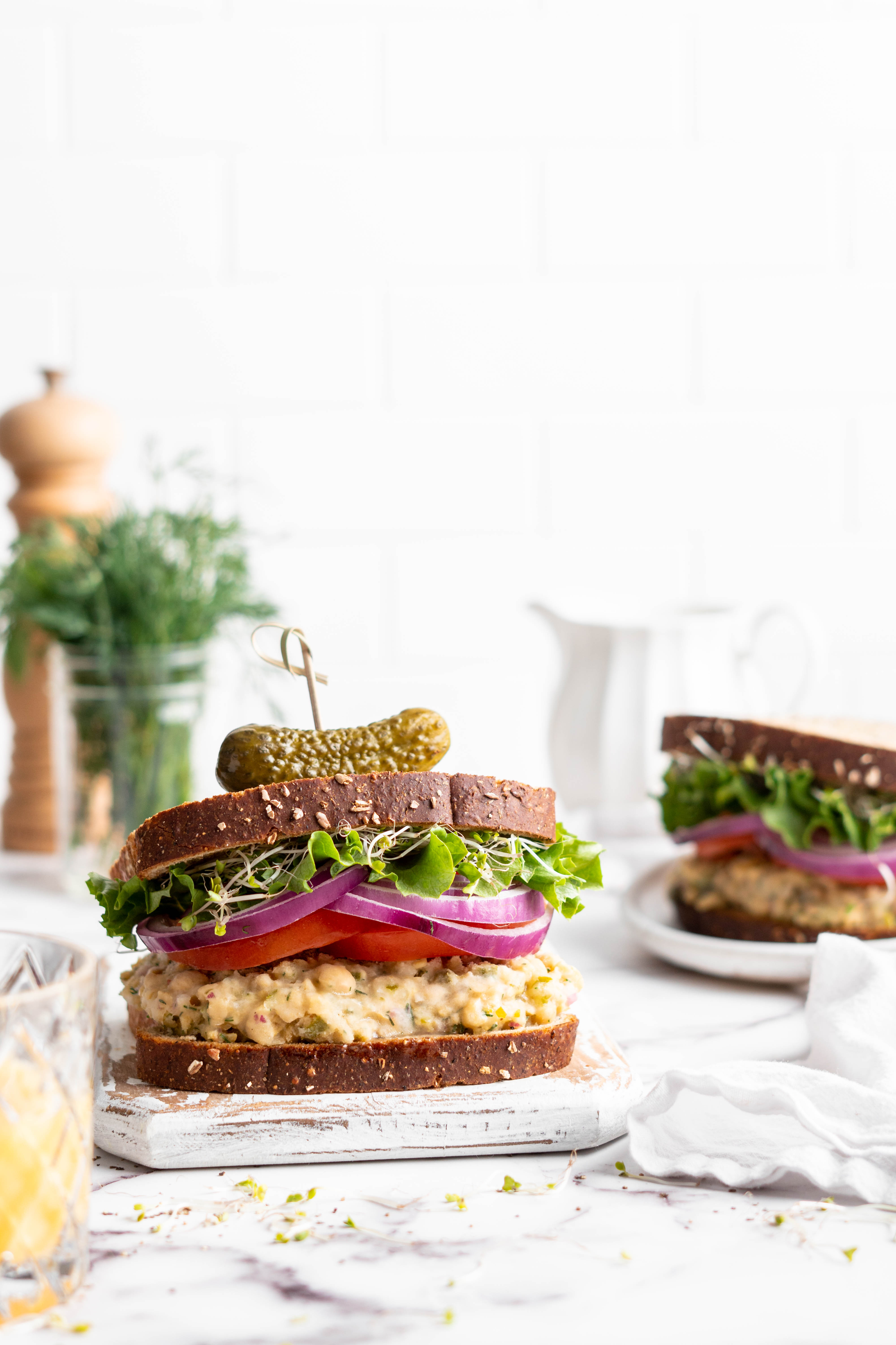 Vegan tuna sandwiches topped with tomatoes, red onions, and sprouts