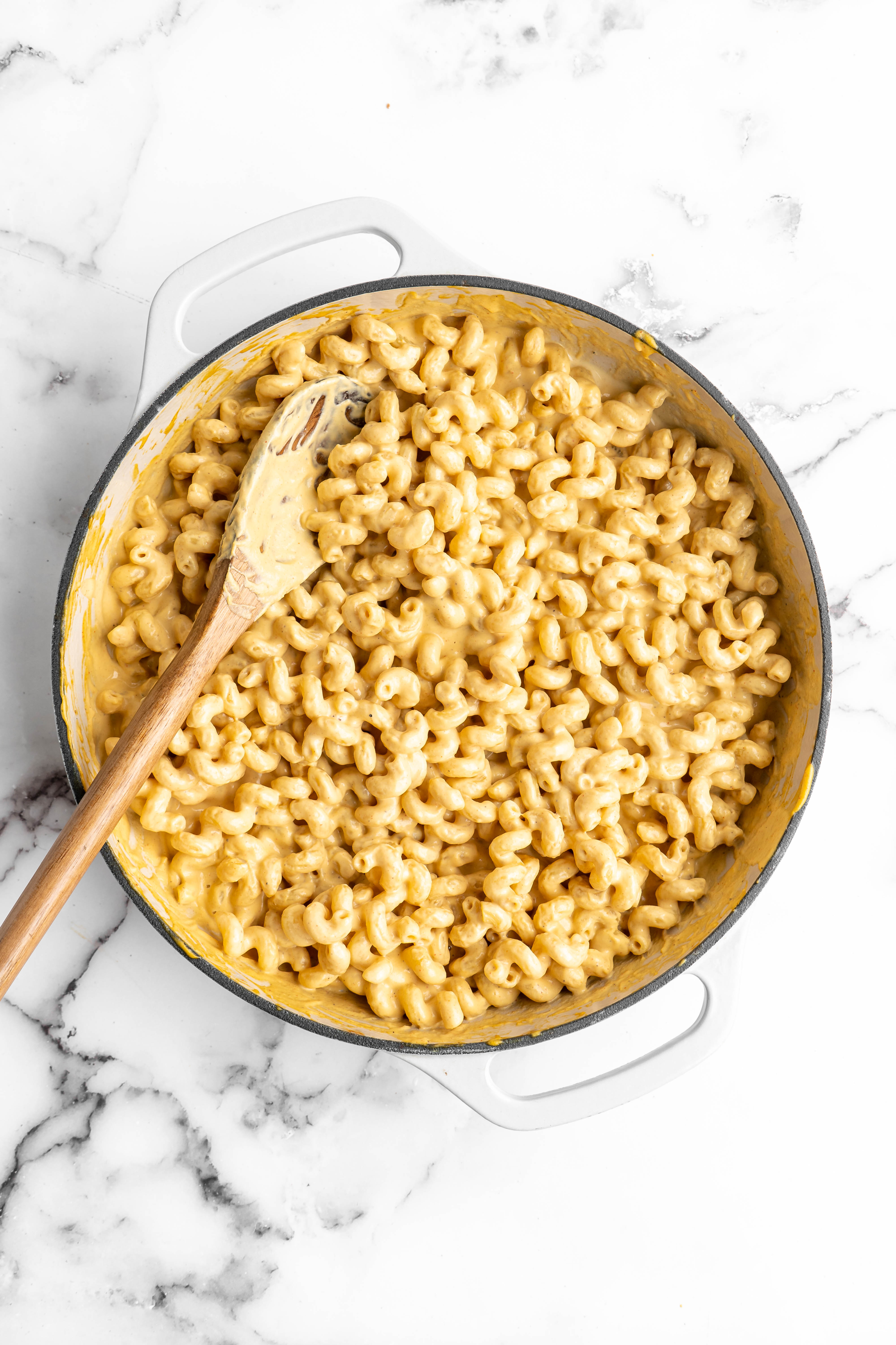 Vegan mac and cheese in pan with wooden spoon