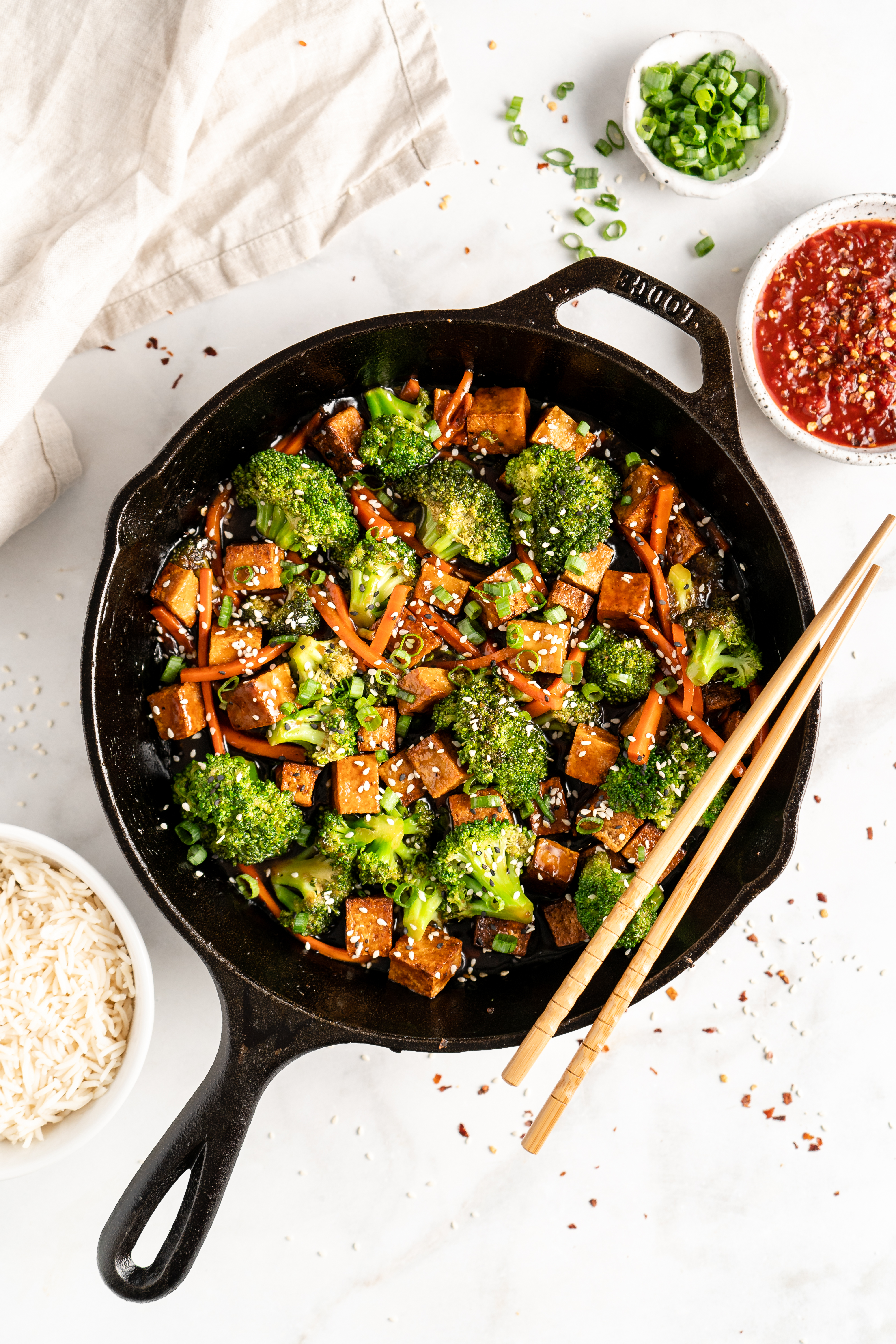 Overhead view of tofu and veggie stir fry in cast iron skillet with chopsticks