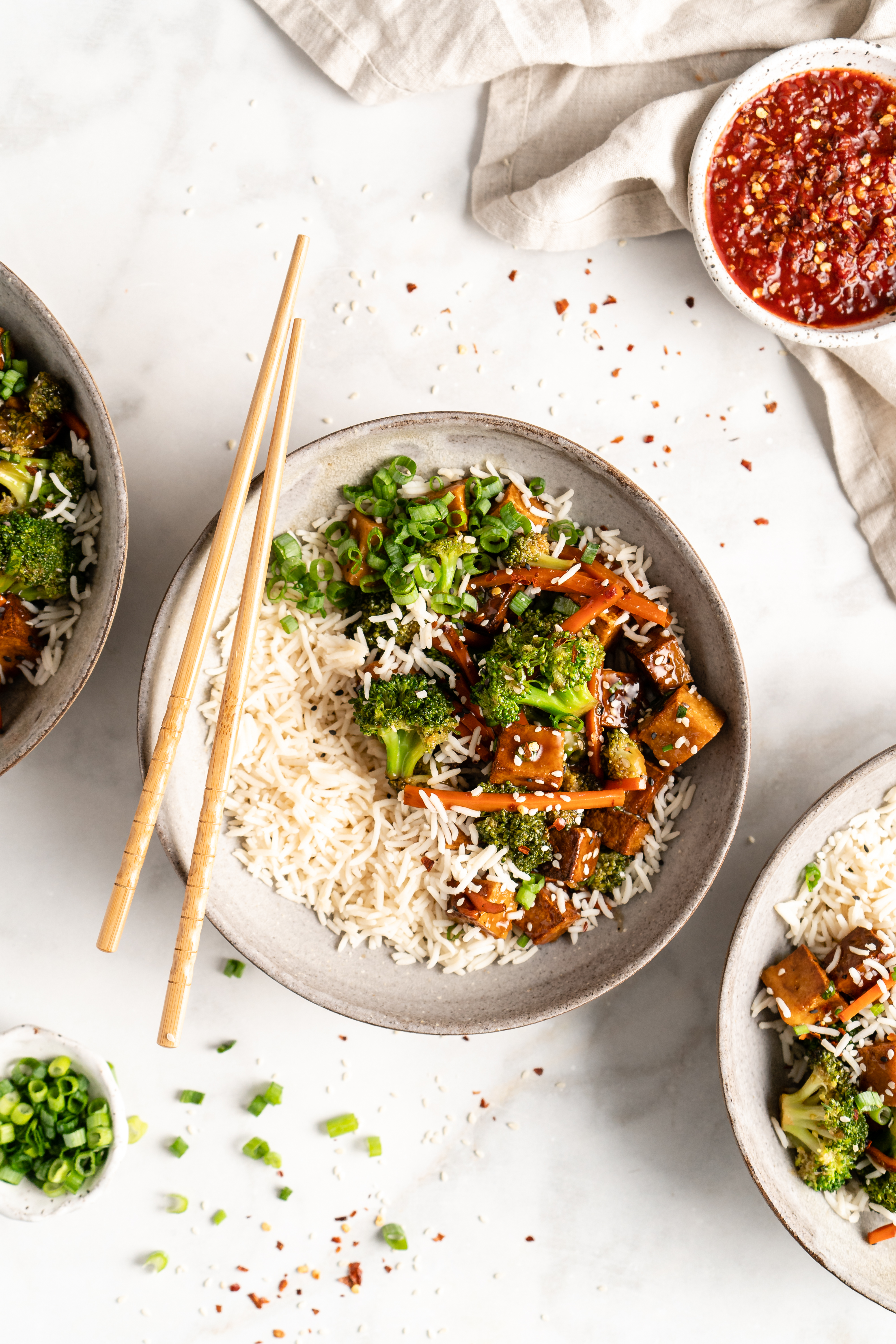Overhead view of tofu and veggie stir fry in bowls with rice and chopsticks