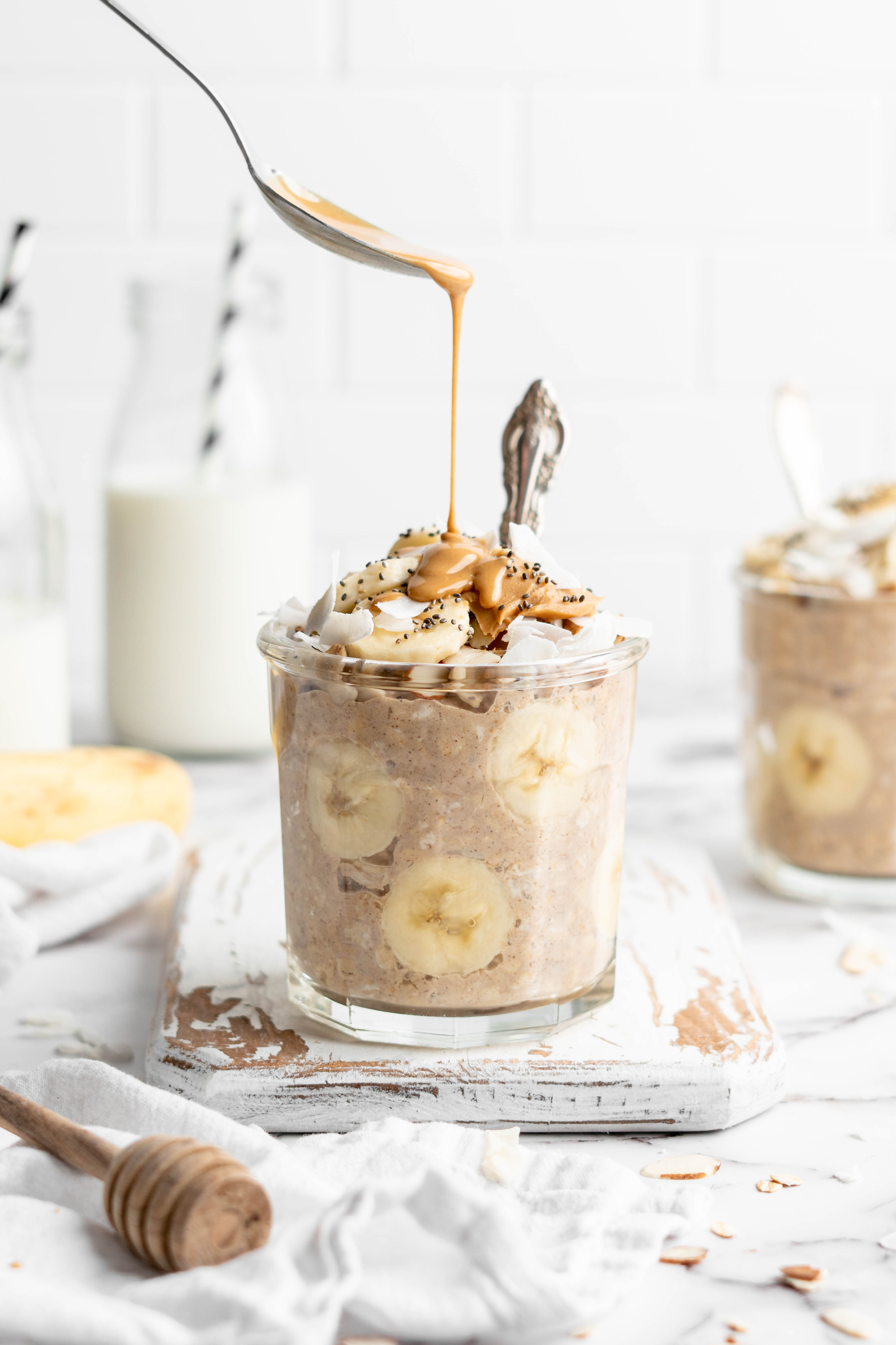 Spooning peanut butter over jar of overnight oats with bananas