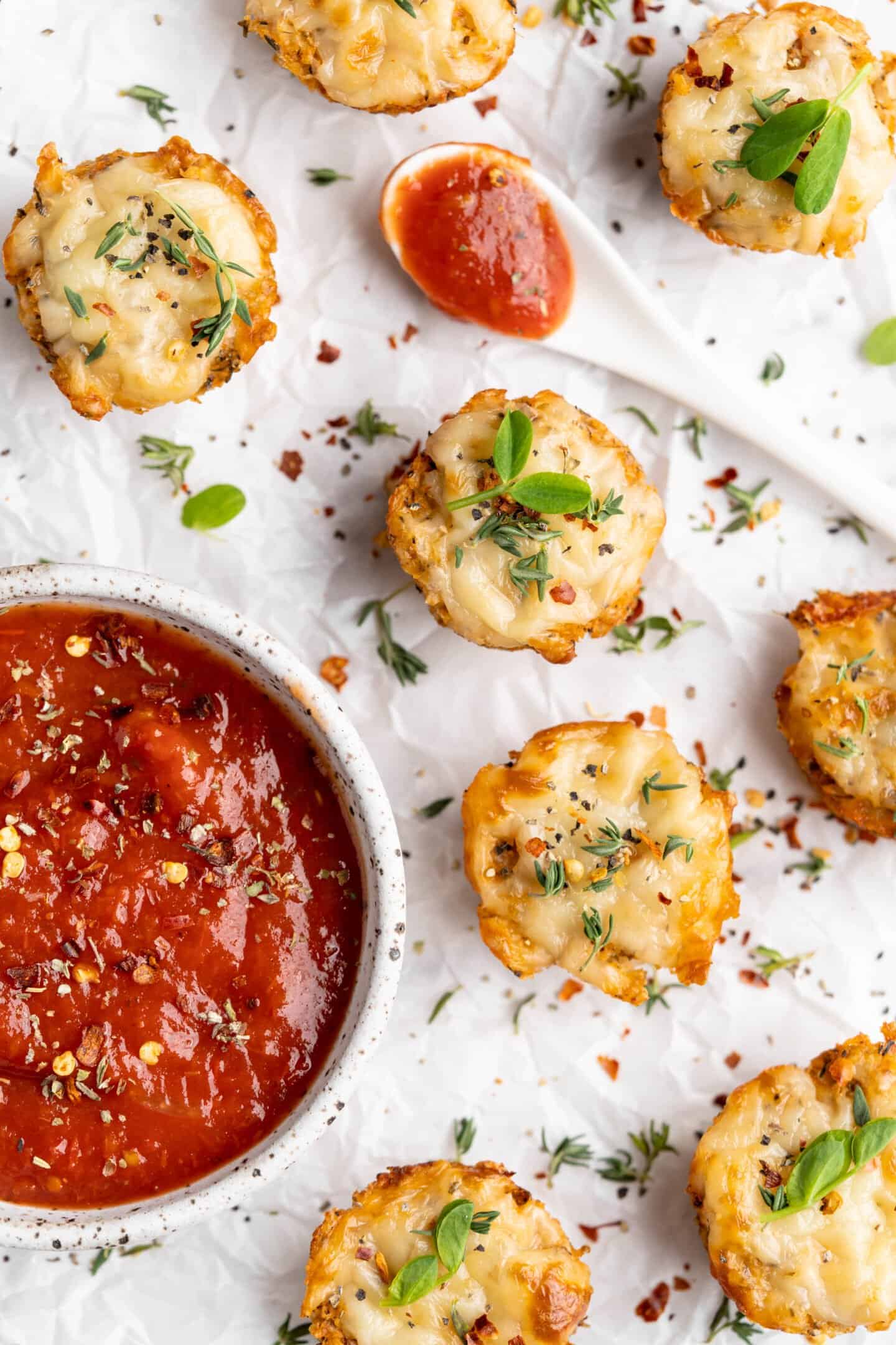 Overhead view of cauliflower pizza bites with bowl and spoon of marinara