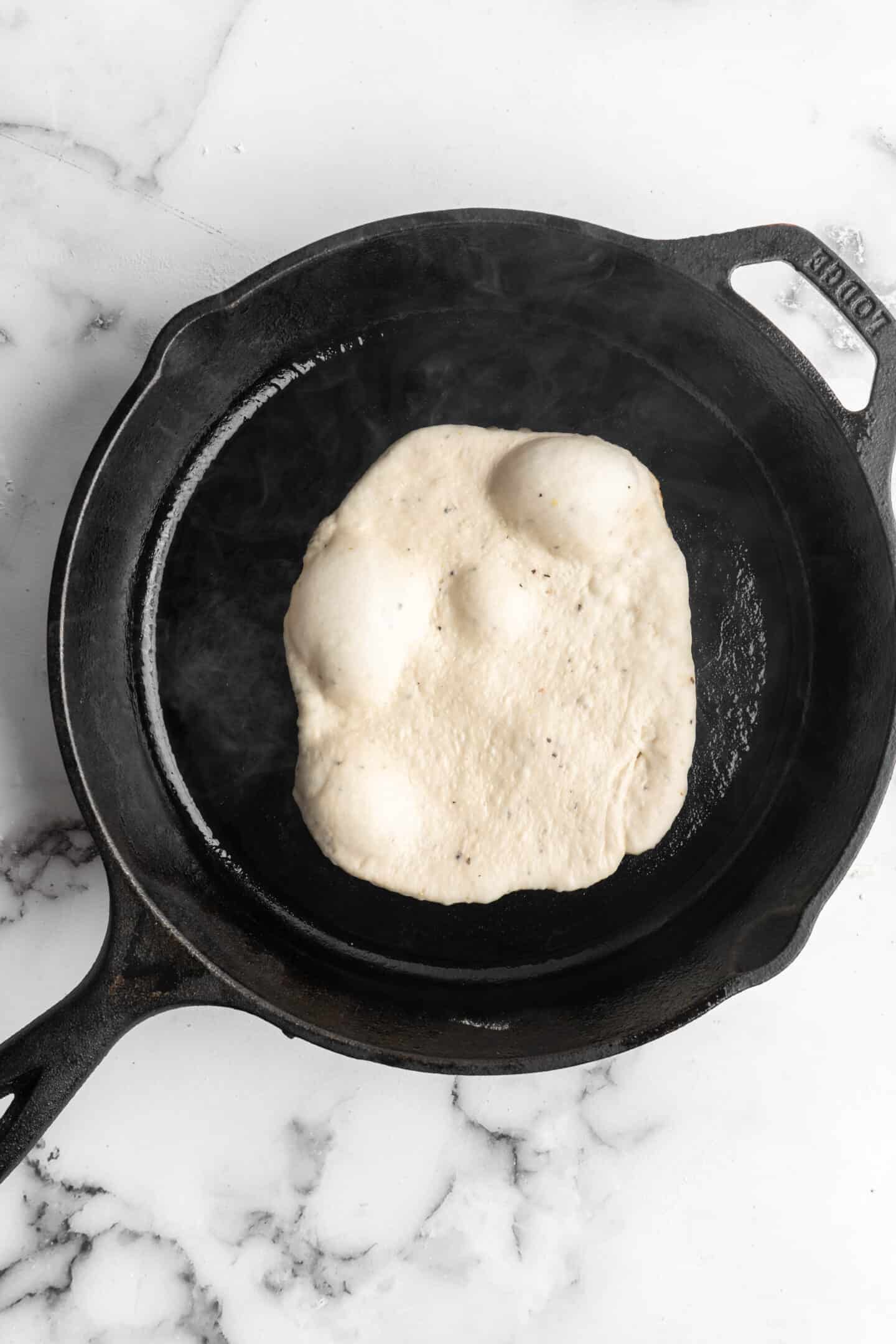 Overhead view of naan cooking in cast iron skillet