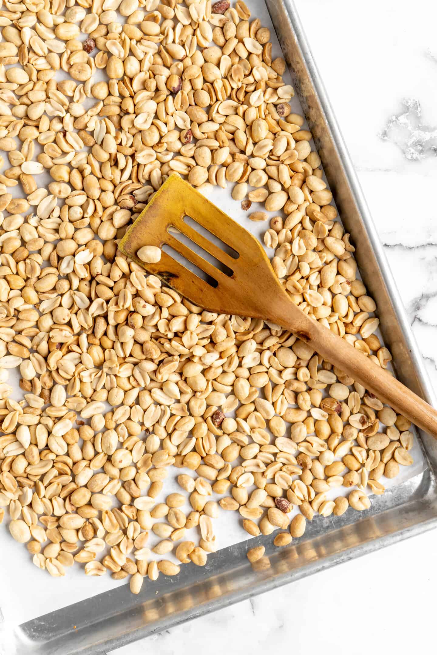 Overhead view of peanuts on baking sheet with wooden spatula