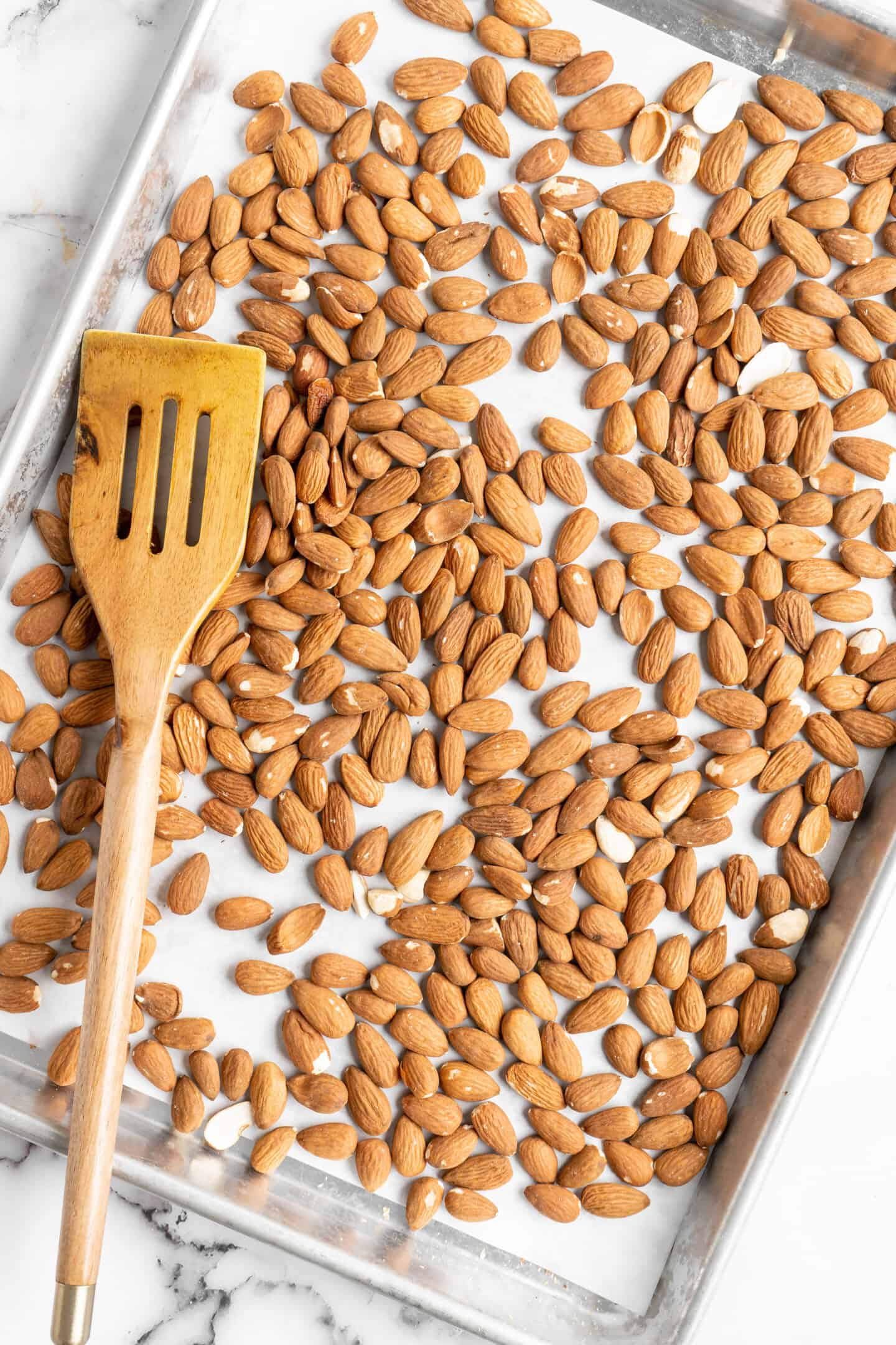 Overhead view of almonds on parchment-lined baking sheet with wooden spatula