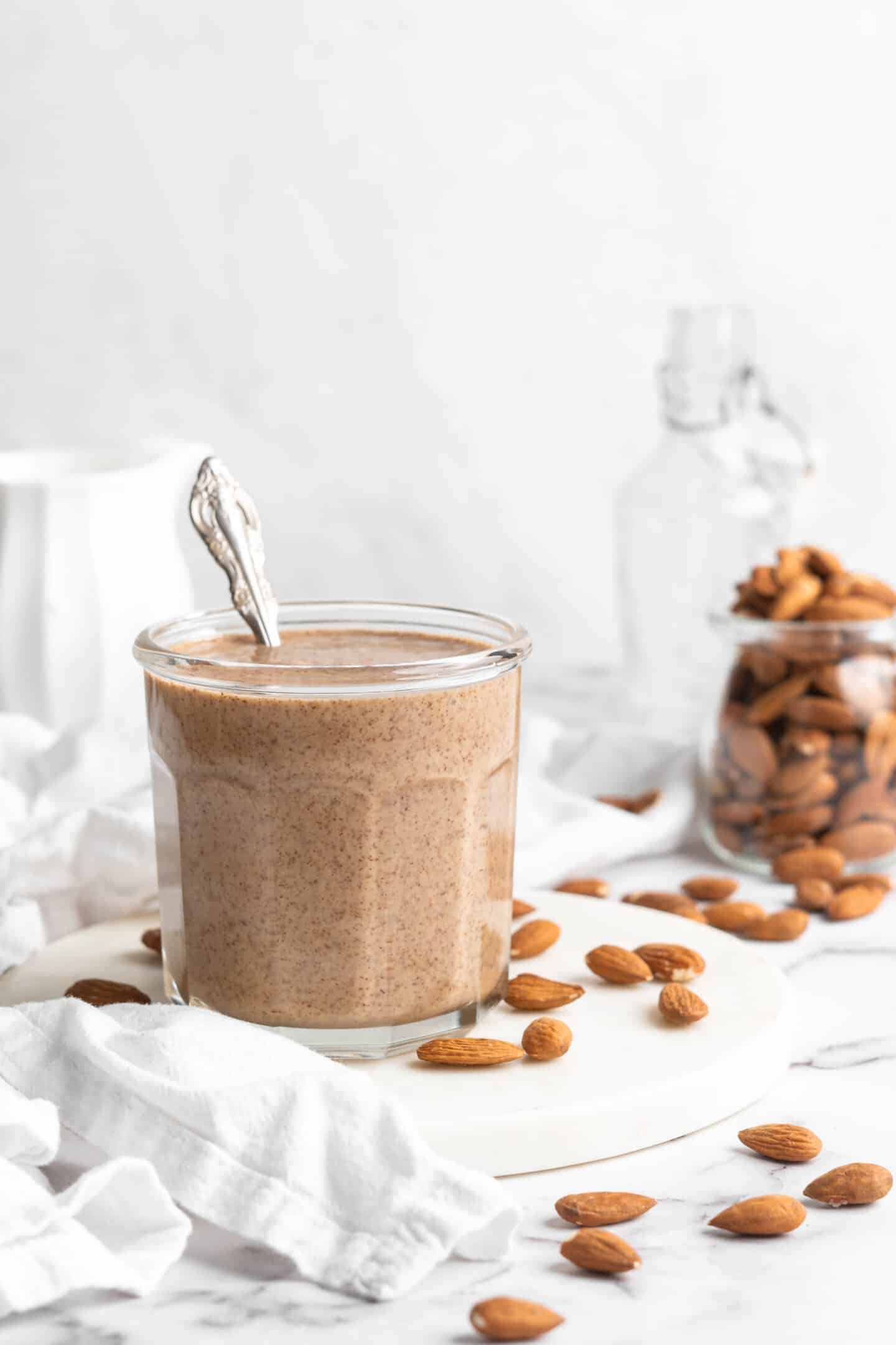 Jar of homemade almond butter with almonds in background