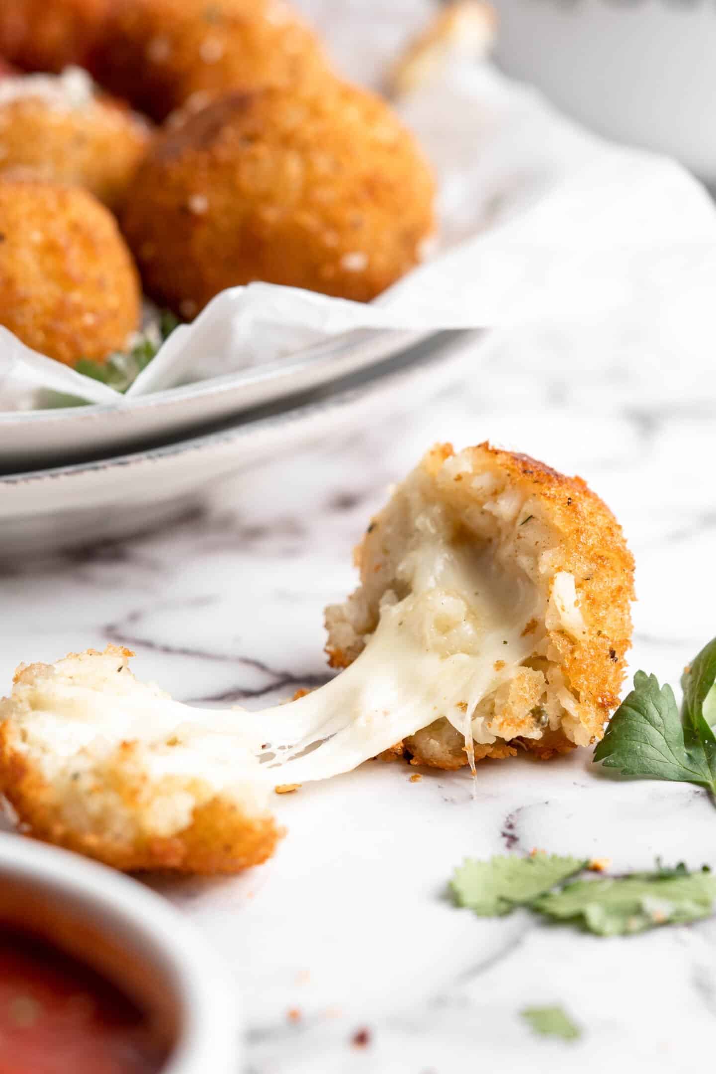 Two halves of an arancini, separated to show stretchy vegan cheese inside