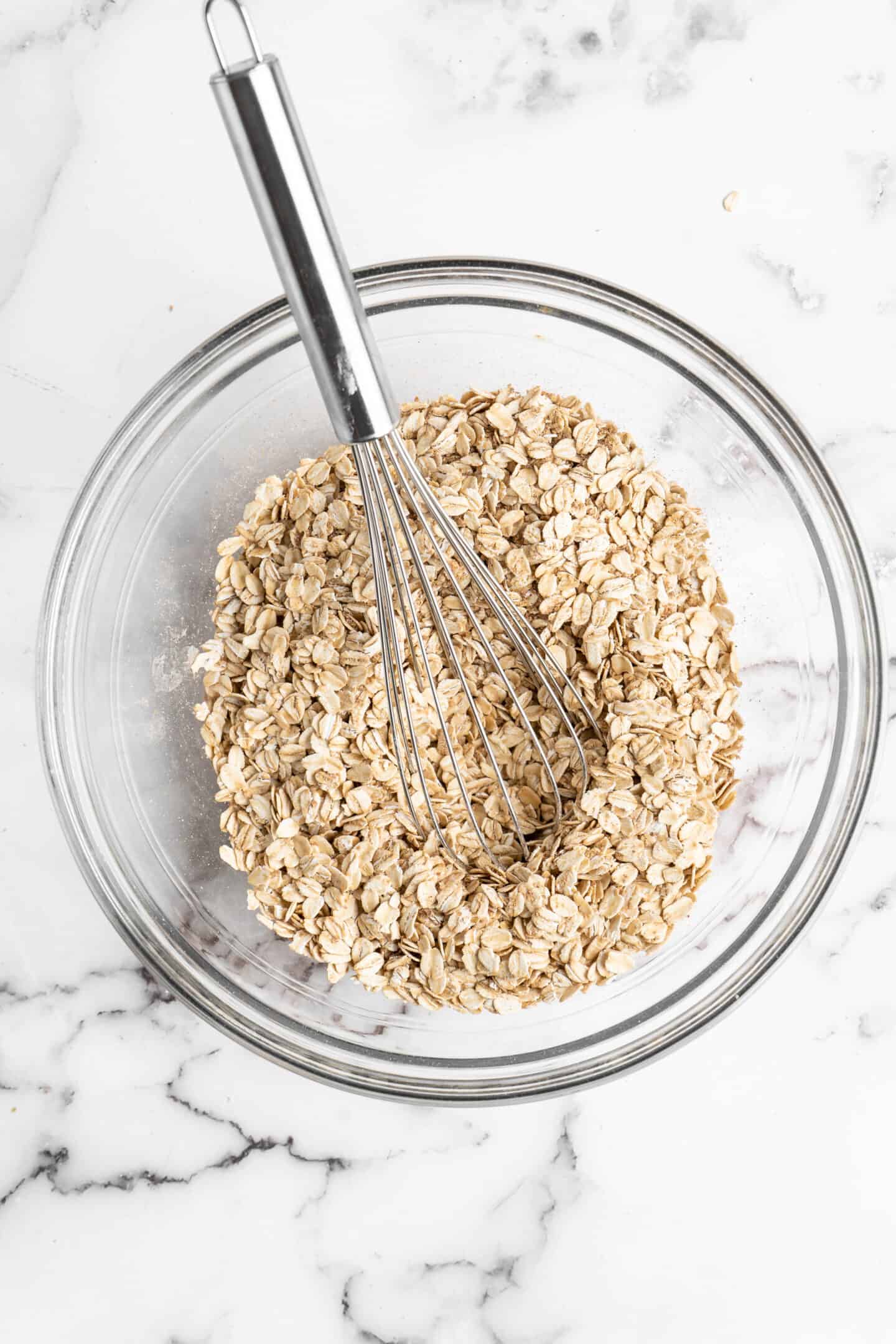 Overhead view of oats in a glass bowl with a whisk.