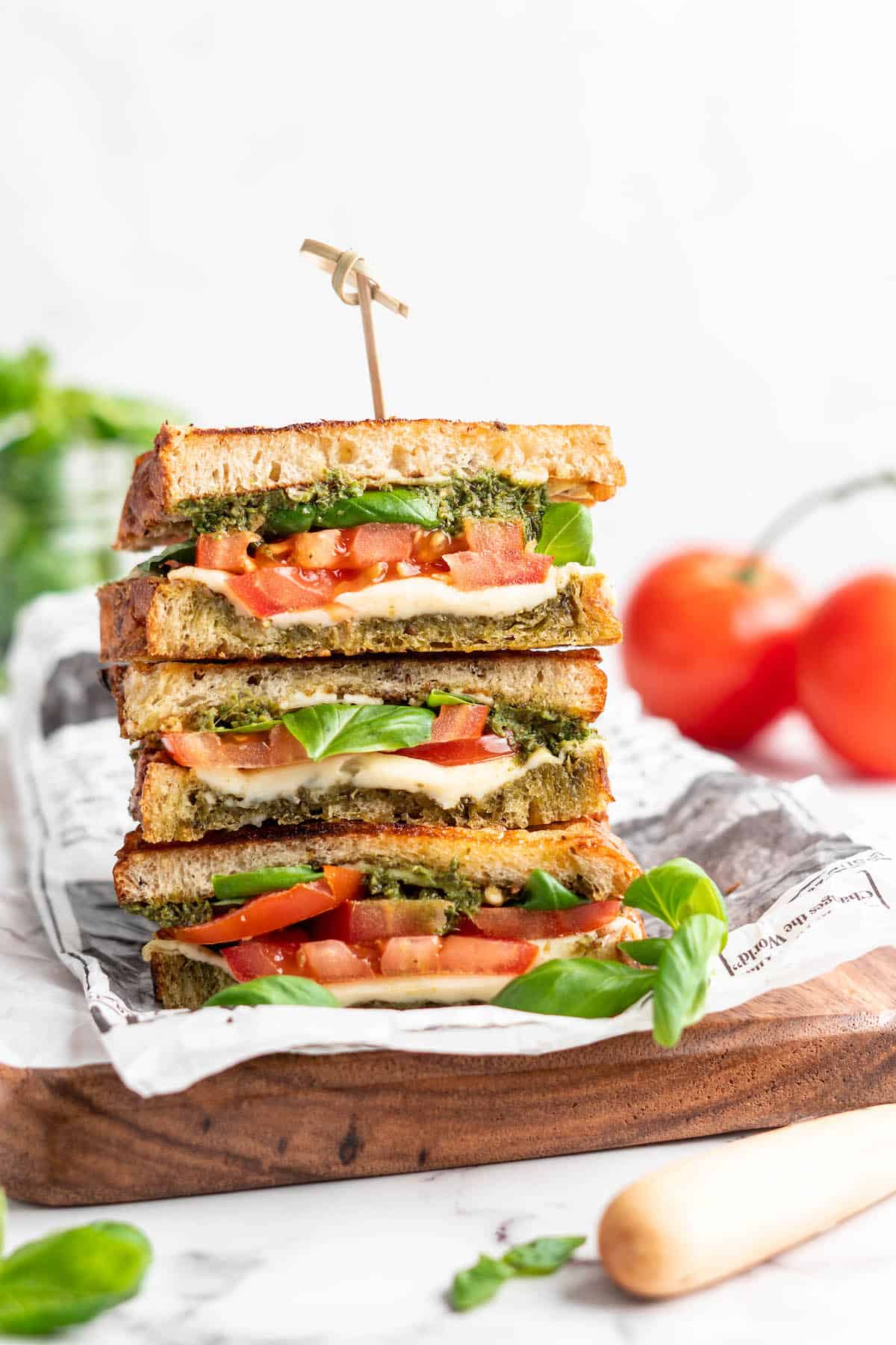 Three stacked vegan caprese sandwiches set on wooden cutting board