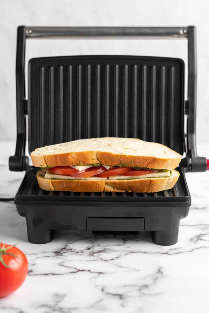 This vegan Caprese sandwich layers plant-based mozzarella with fresh tomatoes and parsley pesto, all on crusty French bread. Best lunch ever! Vegan caprese sandwich on panini press