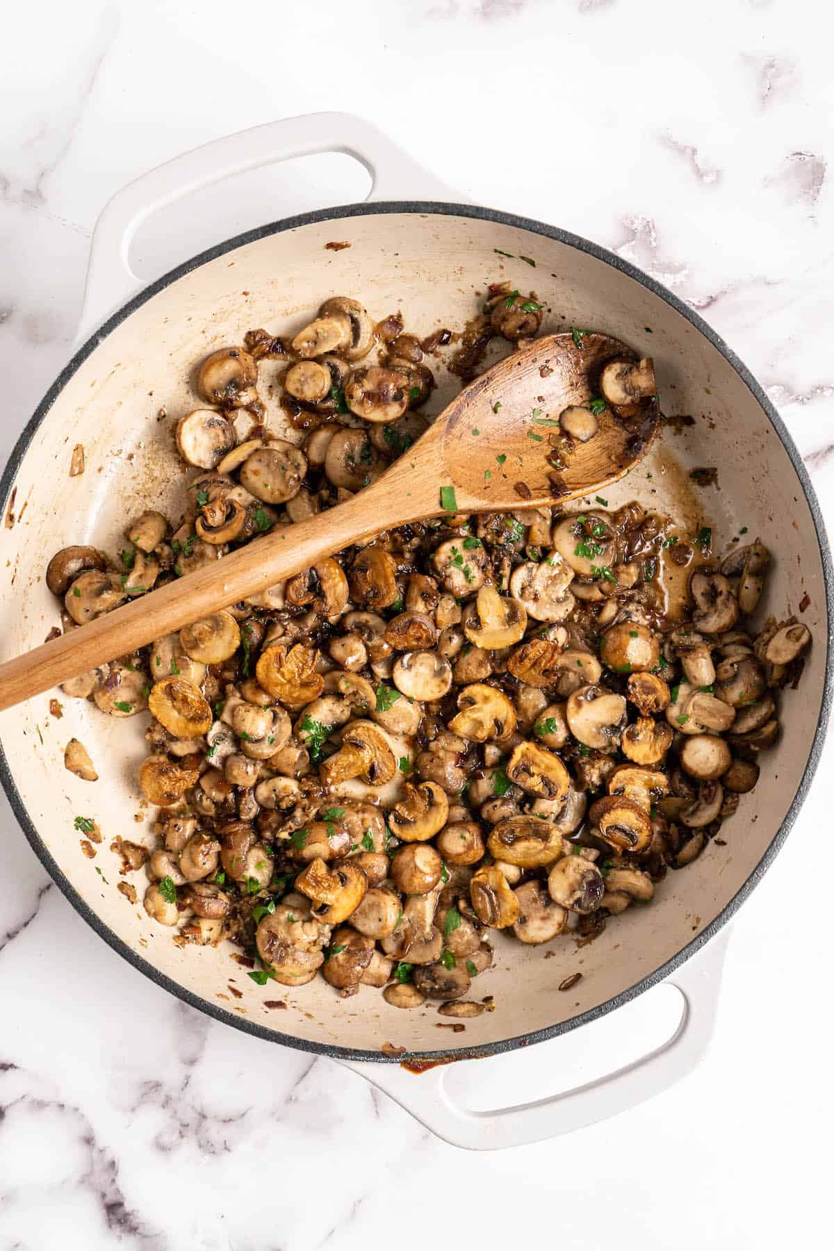 Overhead view of cooked mushrooms in pan with wooden spoon