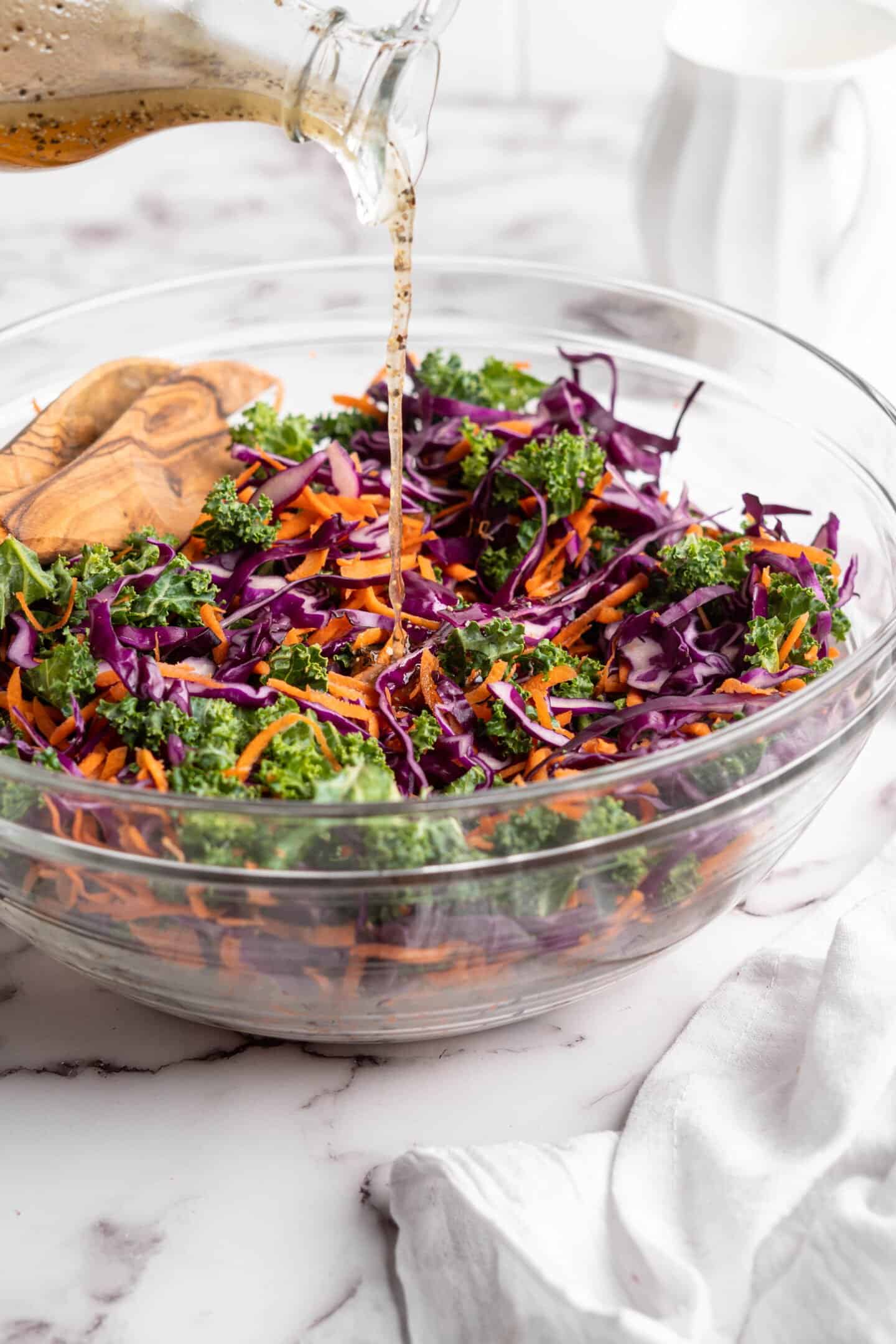 Dressing being drizzled over kale slaw in a glass bowl.