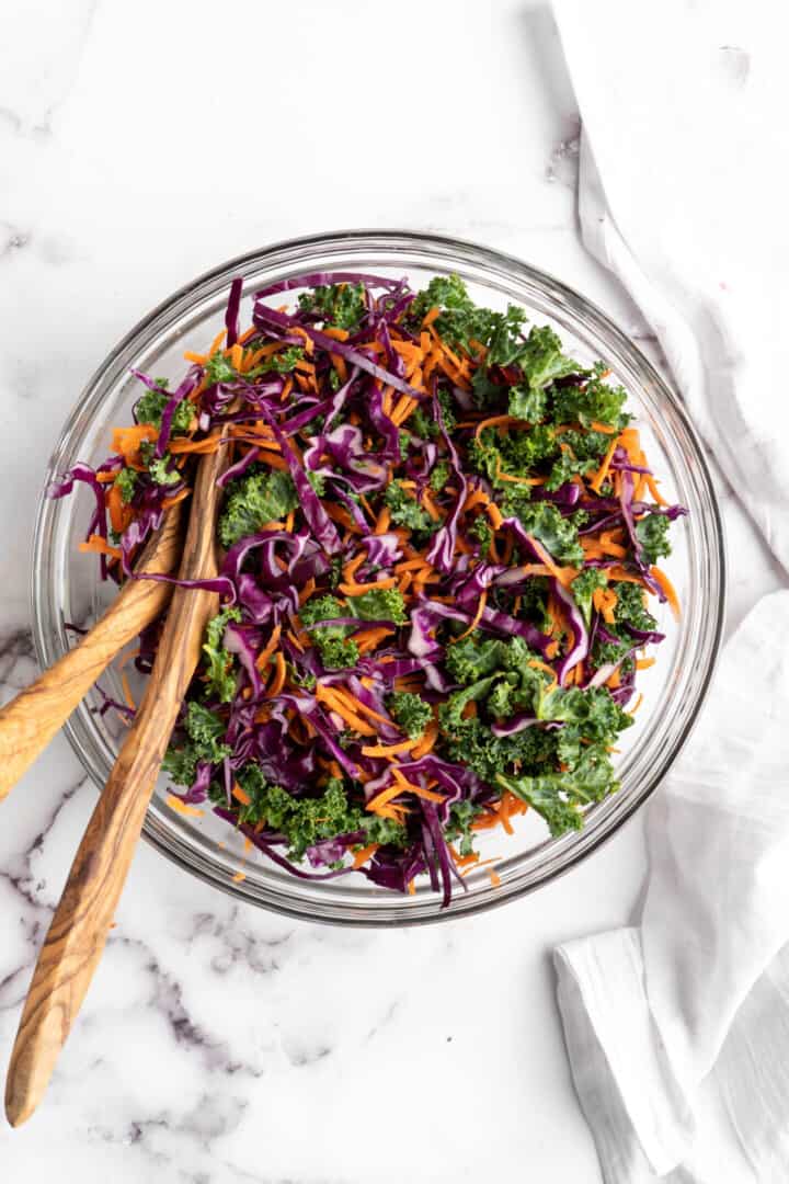 Overhead view of kale slaw in large bowl with two salad tongs.