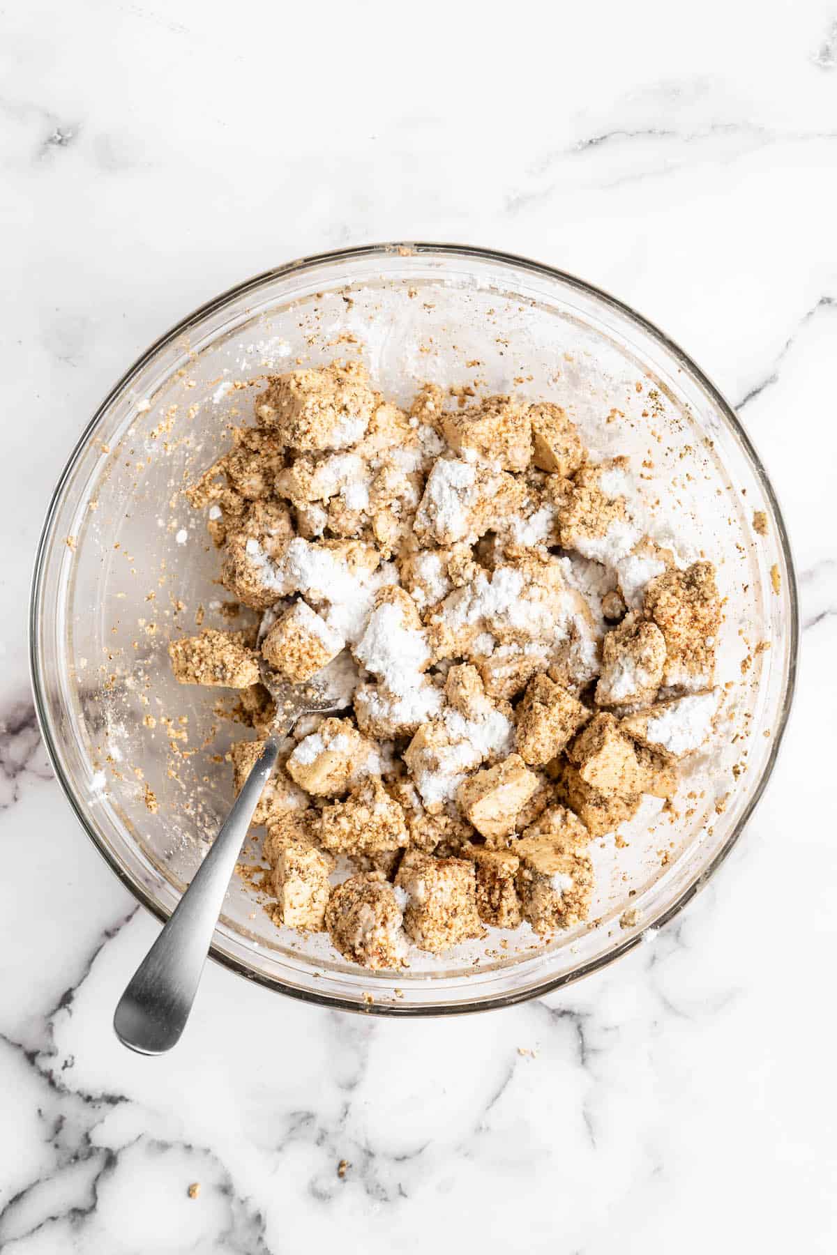 Overhead view of tofu tossed with cornstarch in glass bowl