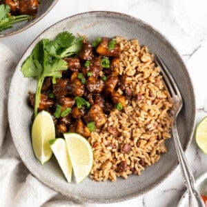 Overhead view of jerk tofu in bowl with rice, lime wedges, and cilantro