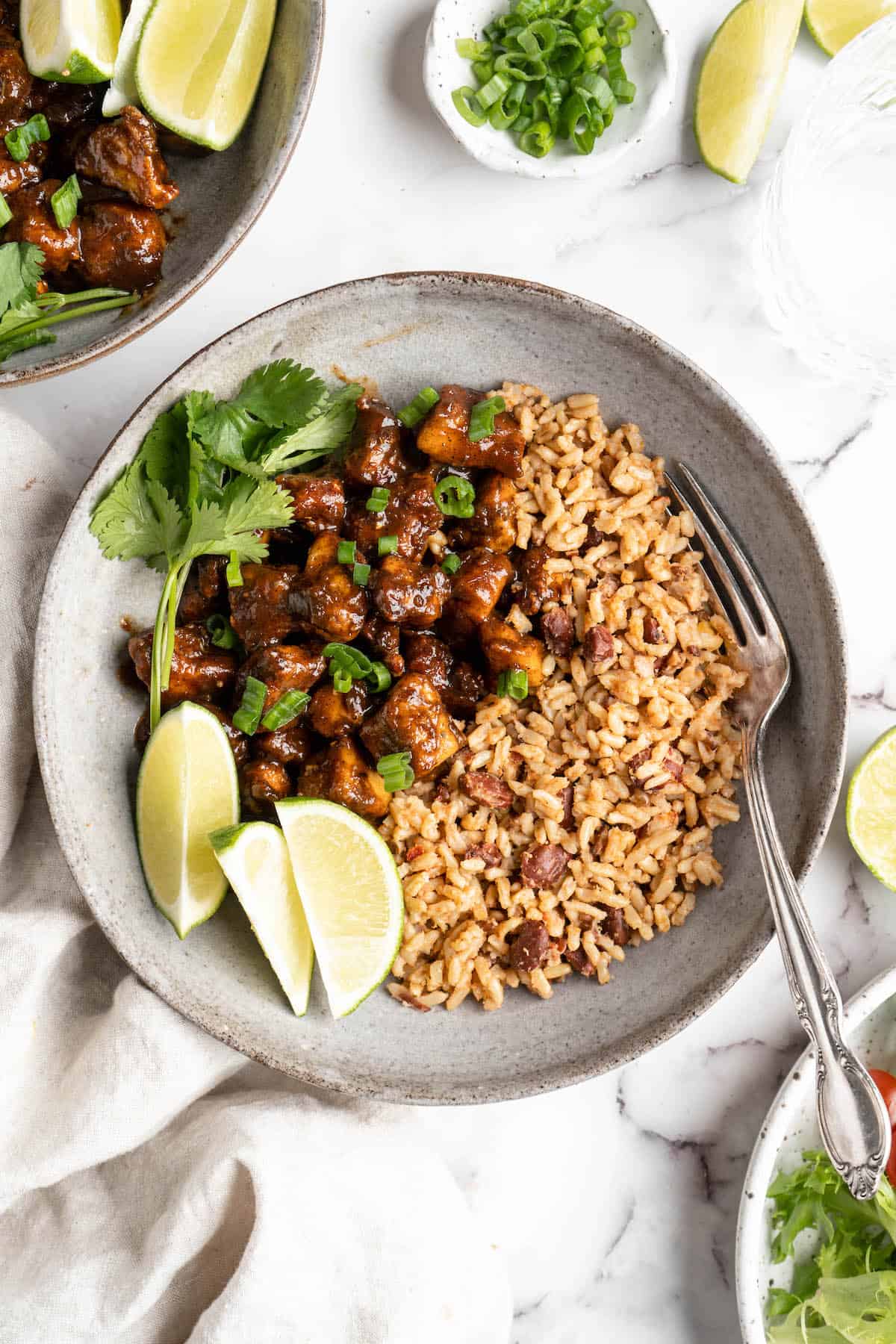 Overhead view of jerk tofu in bowl with rice, lime wedges, and cilantro