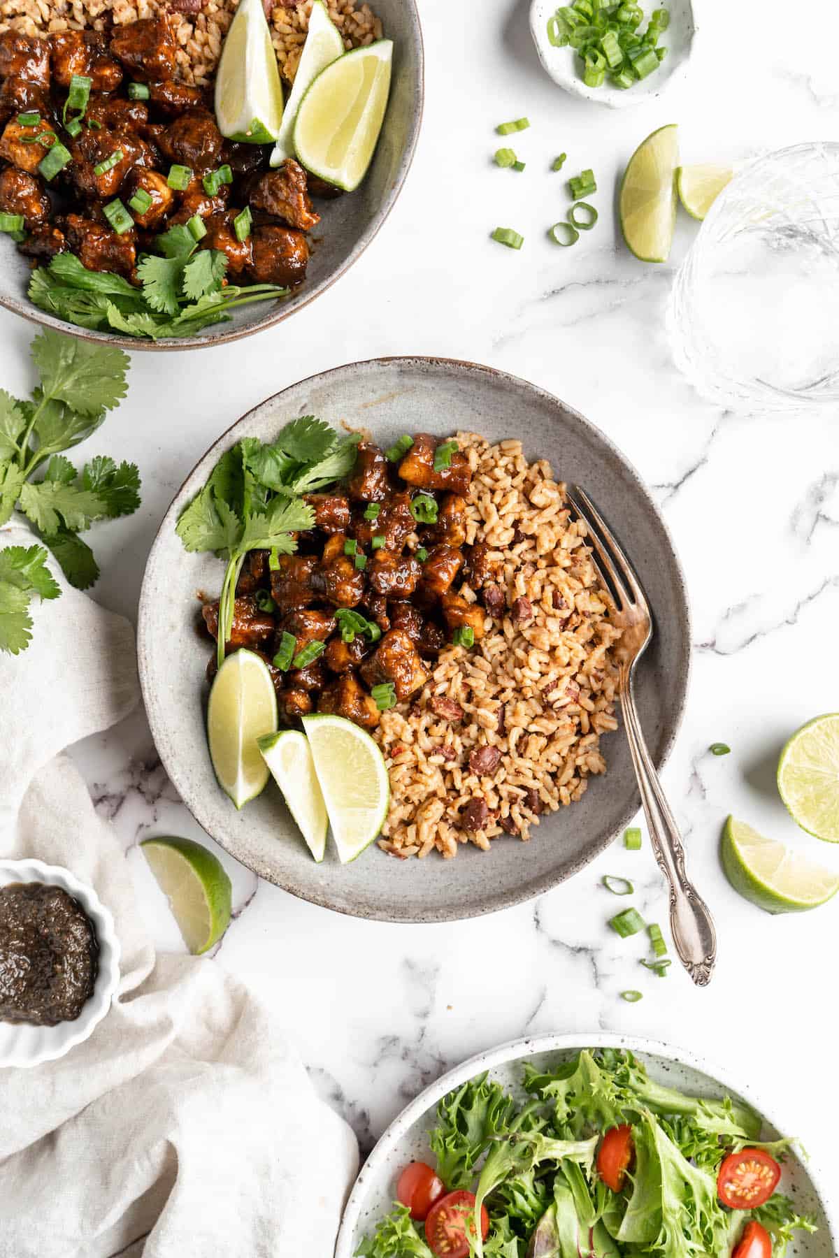 Overhead view of jerk tofu in bowls with rice and lime wedges