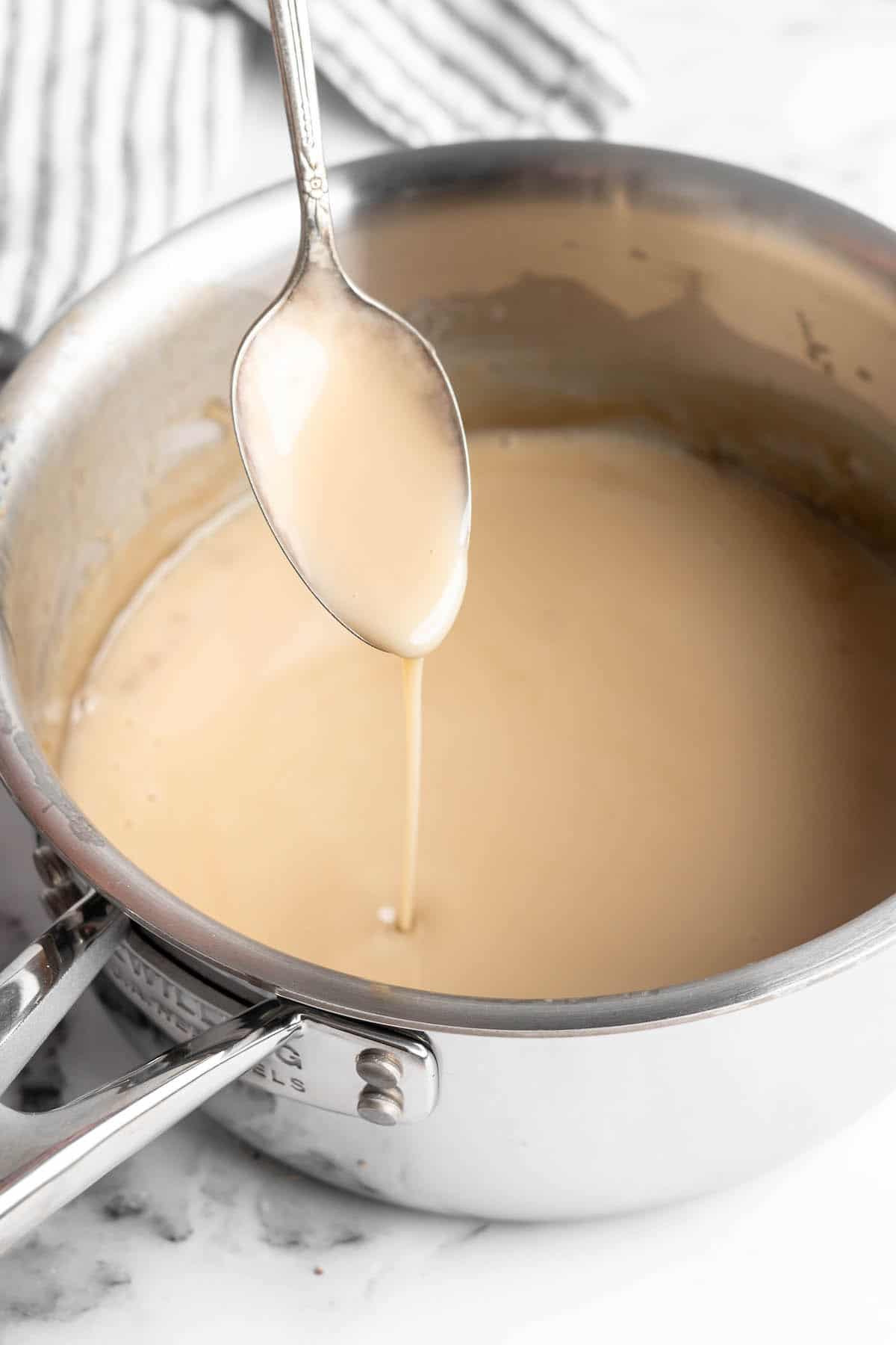 Spoon drizzling vegan condensed milk into saucepan