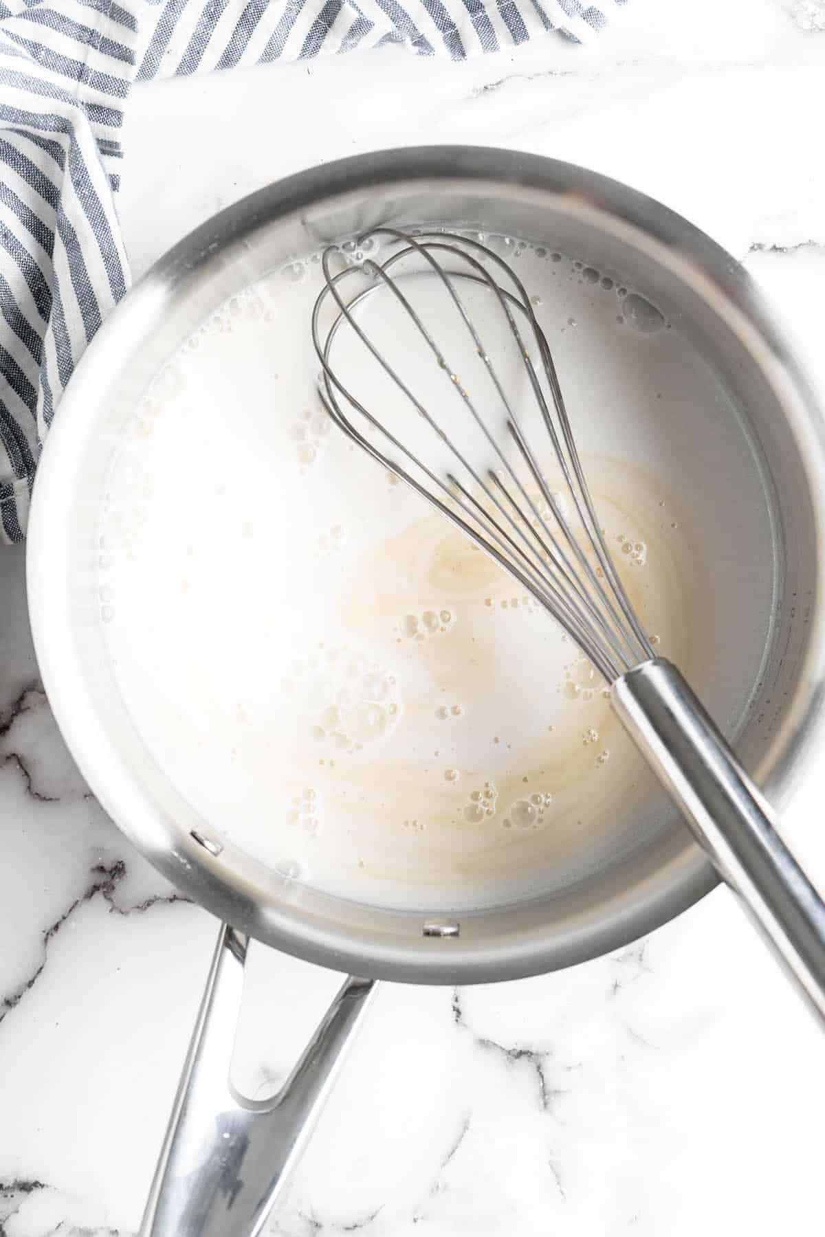 Overhead view of coconut milk and maple syrup in pan with whisk