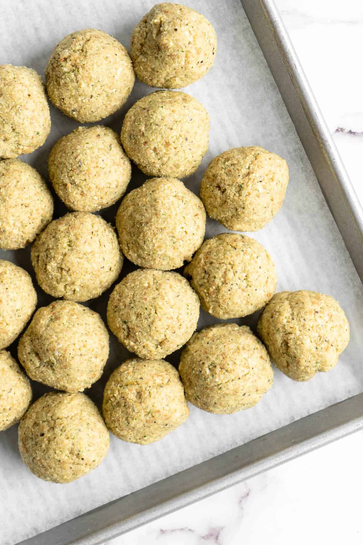 Uncooked vegan meatballs on parchment lined sheet pan