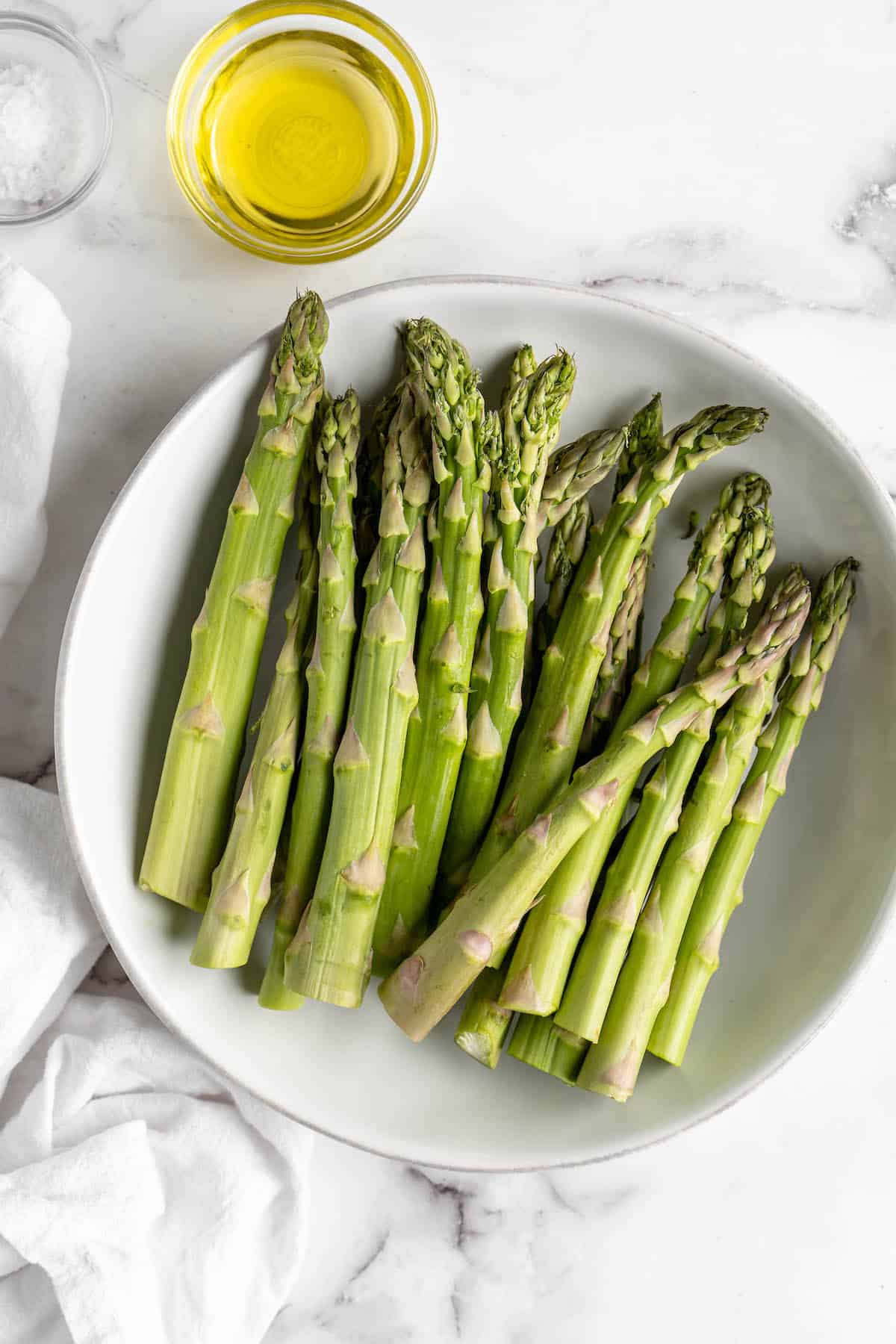 Overhead view of asparagus in bowl with small bowl of olive oil