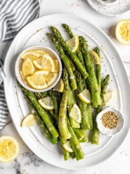 Overhead view of air fryer asparagus on platter with bowl of lemon wedges