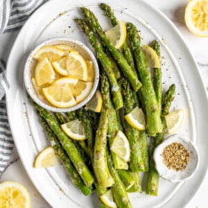 Overhead view of air fryer asparagus on platter with bowl of lemon wedges