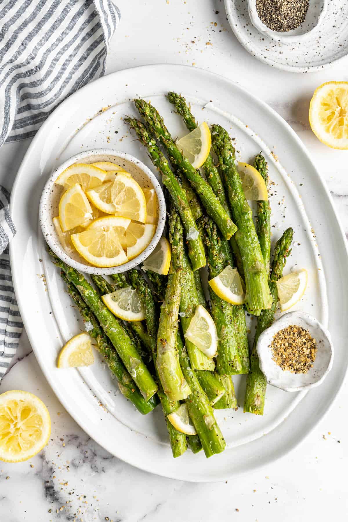 Overhead view of air fryer asparagus on platter with bowl of lemon wedges