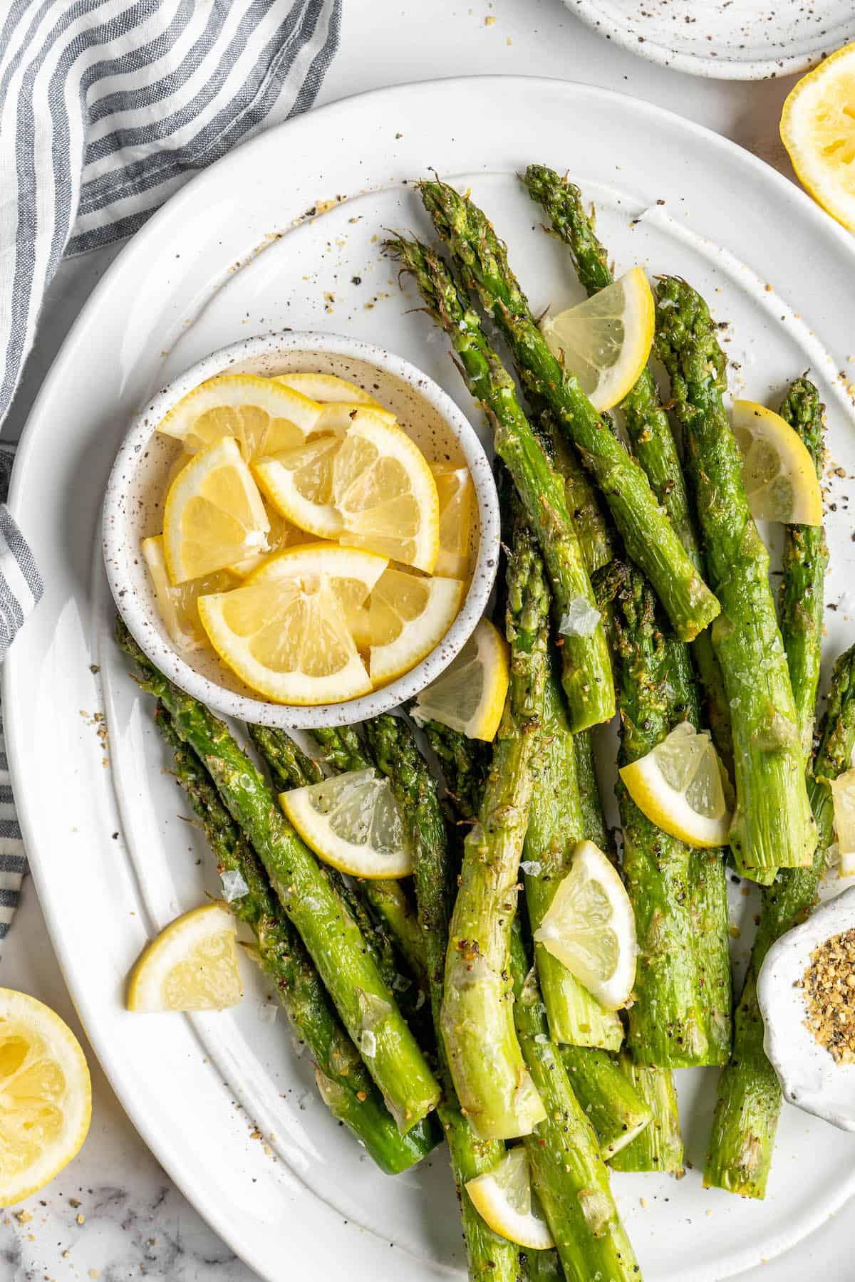 Overhead view of air fryer asparagus on serving platter with bowl of lemon wedges