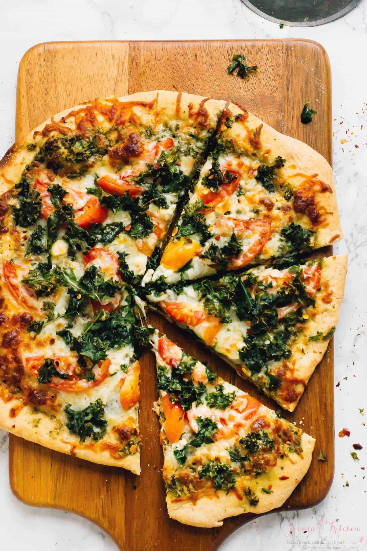 Overhead view of kale pizza on wood cutting board