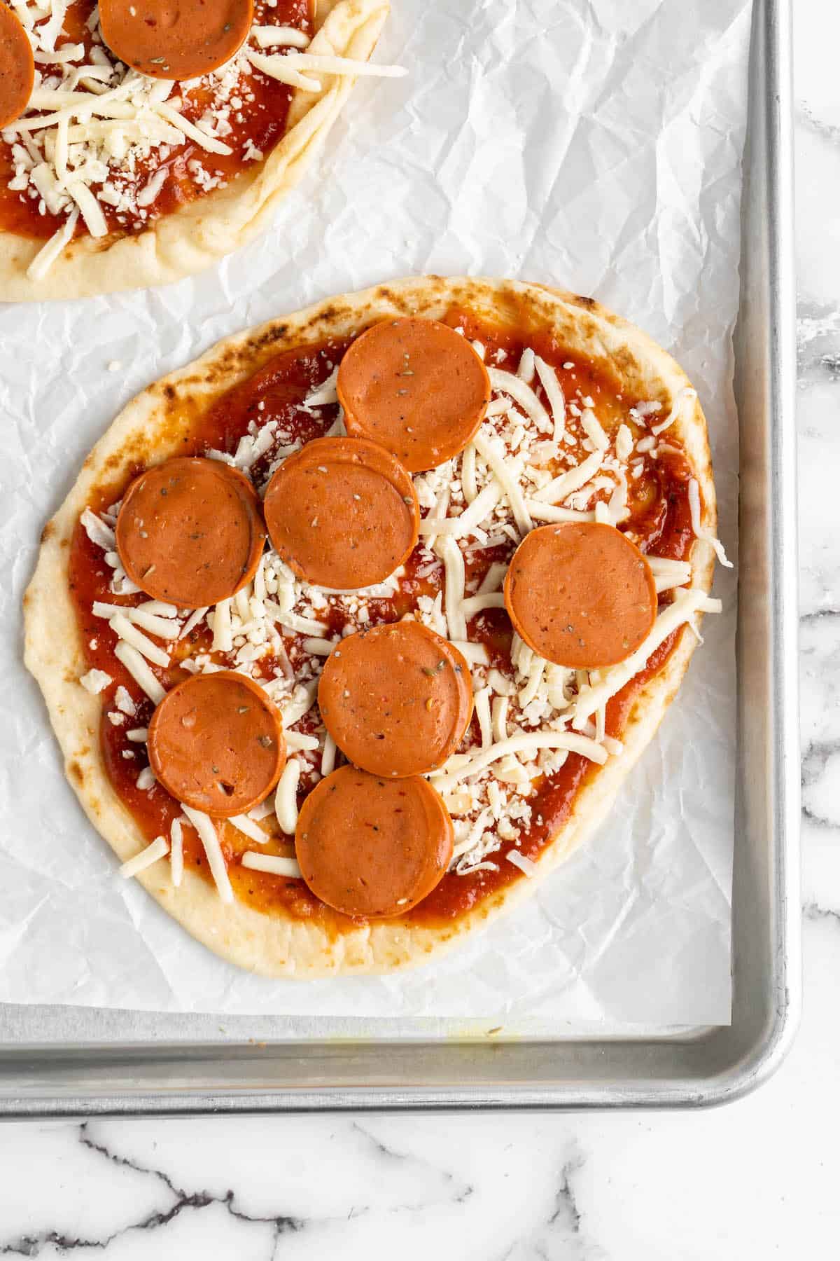 Overhead view of vegan naan pizza with pepperoni on sheet pan