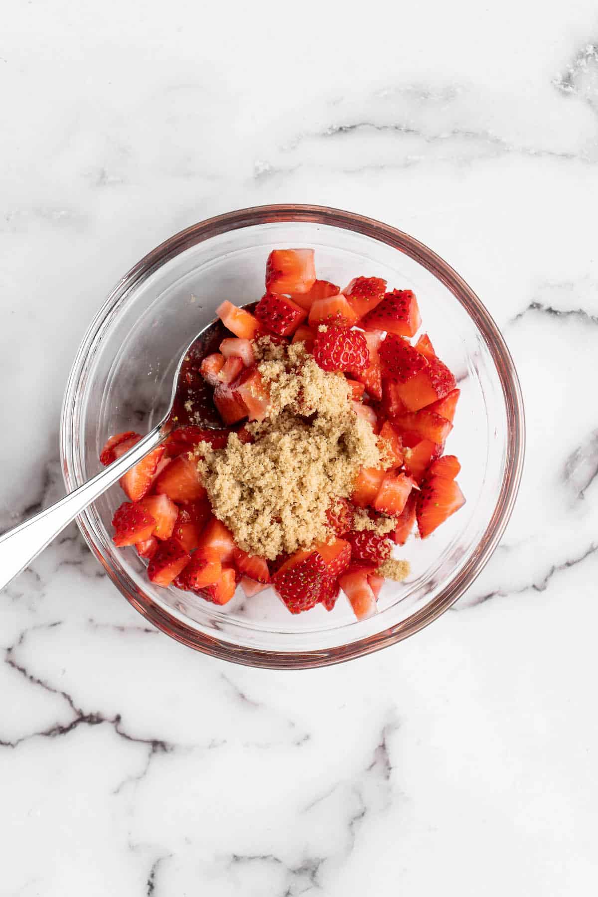 Overhead view of strawberries and brown sugar in glass bowl with spoon