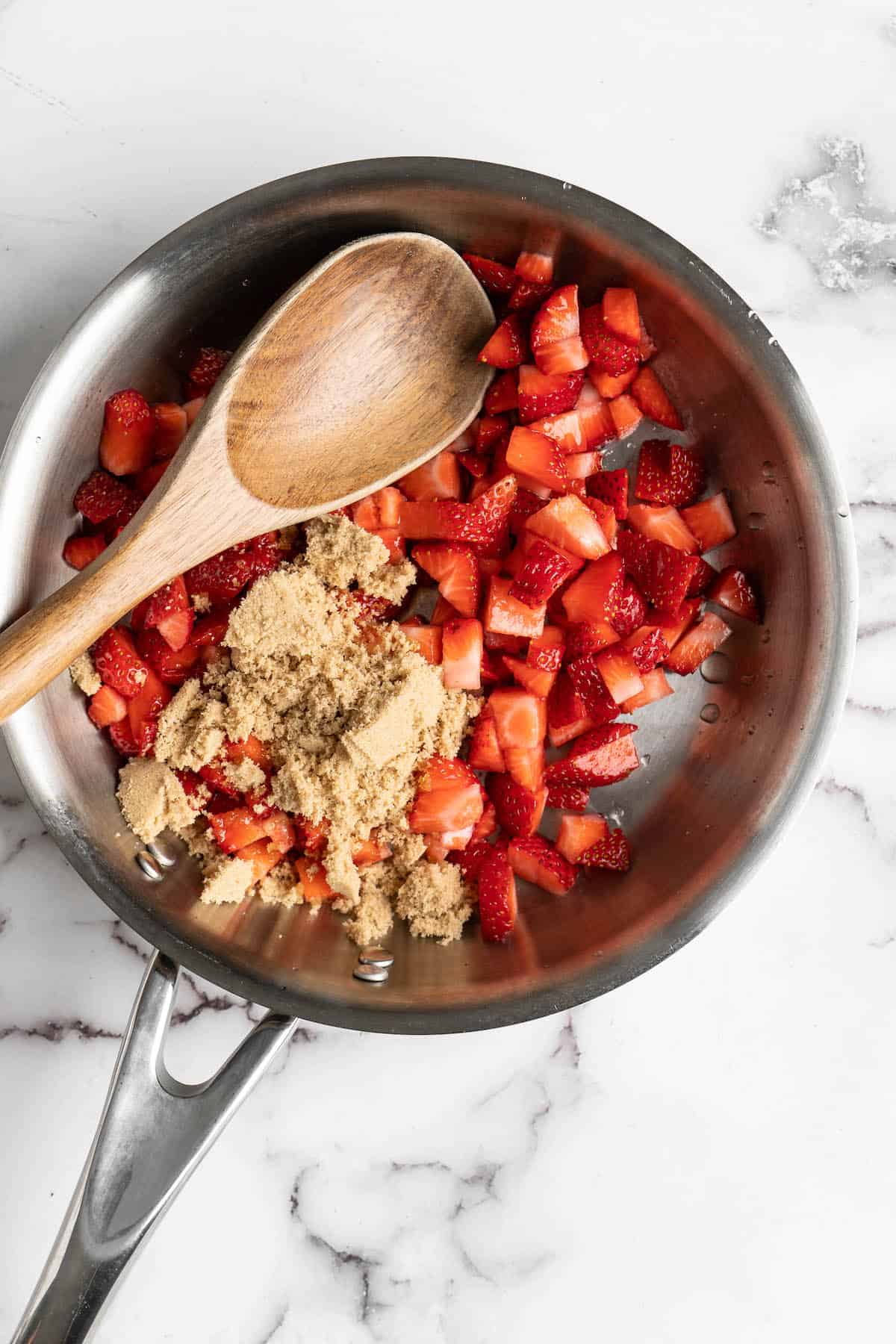 Overhead view of strawberries and brown sugar in pan with wooden spoon