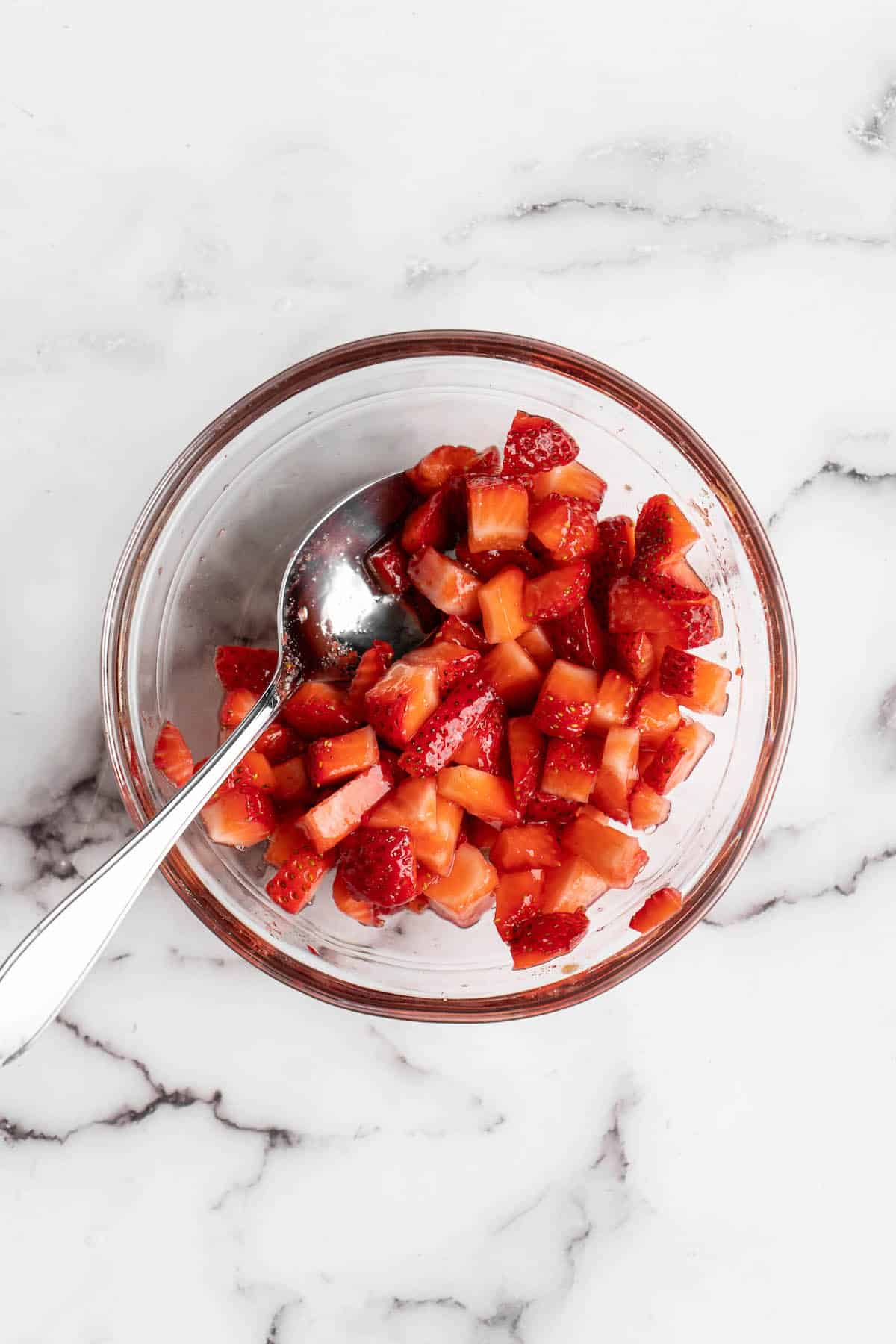 Overhead view of macerated strawberries in glass bowl with spoon