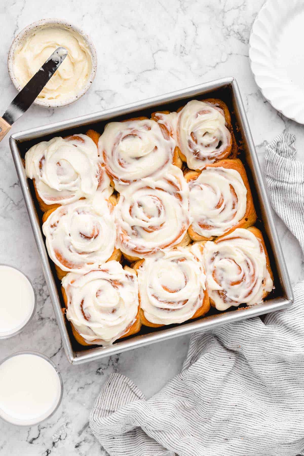 Overhead view of vegan cinnamon rolls in square pan with bowl of frosting